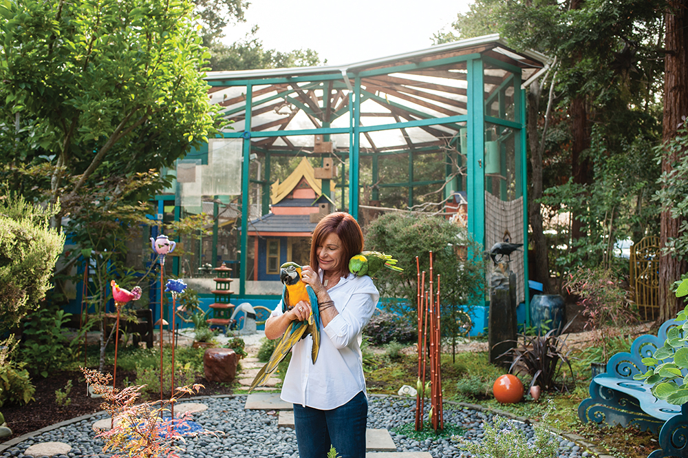 Michele Raffin holds Tico, a blue and gold macaw, while Shana, a yellow-naped Amazon parrot, perches on her shoulder.