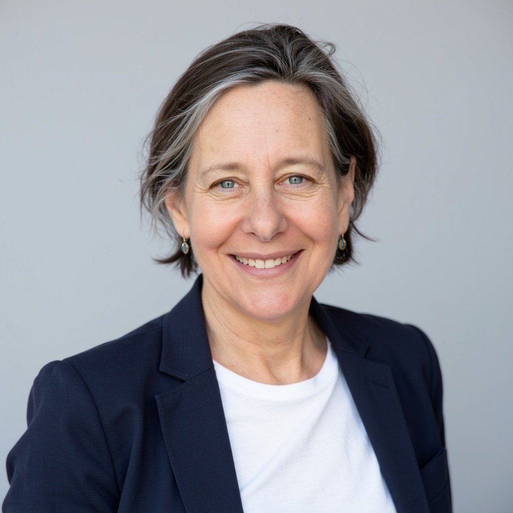 A portrait of a smiling middle-aged woman with short gray hair, wearing a navy blazer and earrings, against a light gray background.