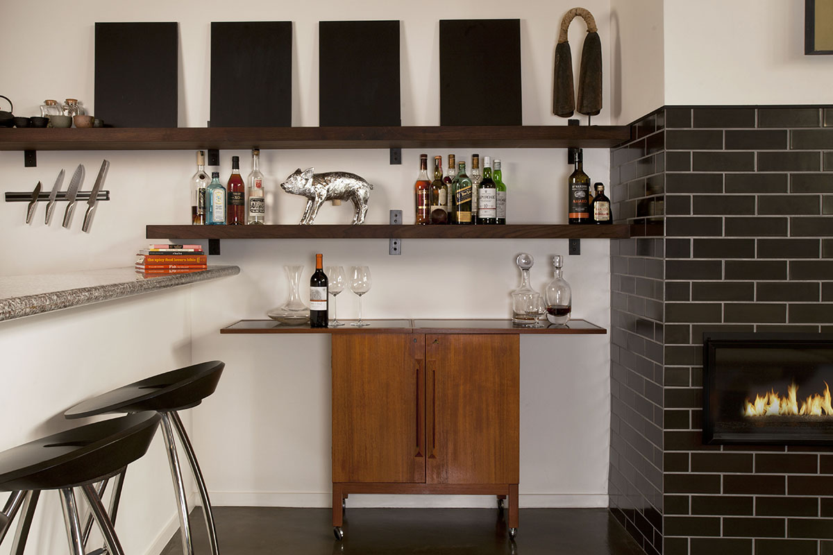 Side bar near dining and living area with fireplace framed by black ceramic tiles from Heath ceramics .