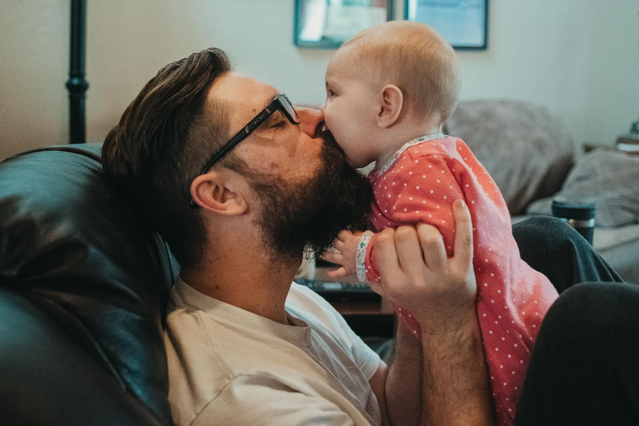 Dad with beard and glasses kissing 6 month old daughter in pajamas
