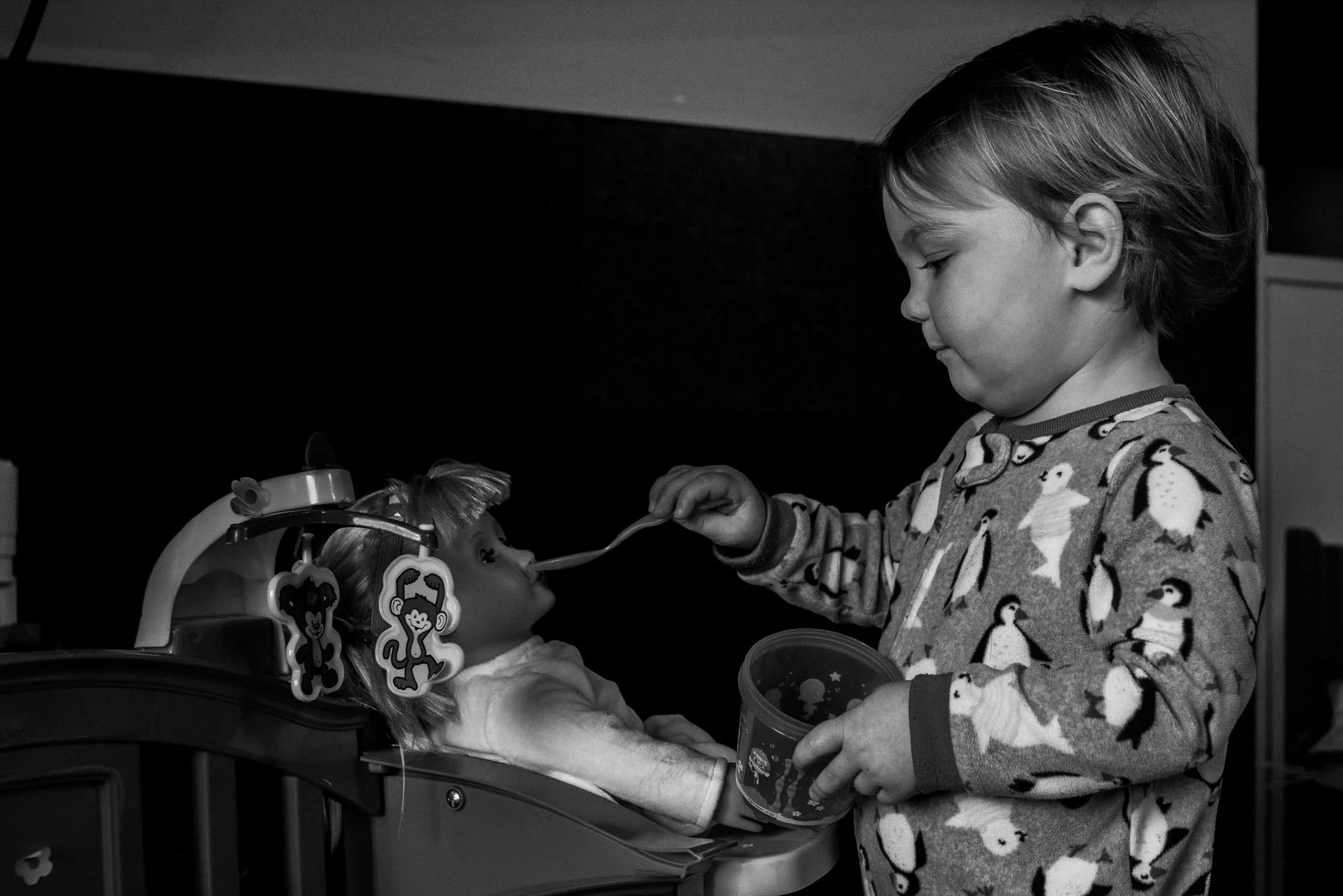 Toddler in penguin pajamas feeding baby doll