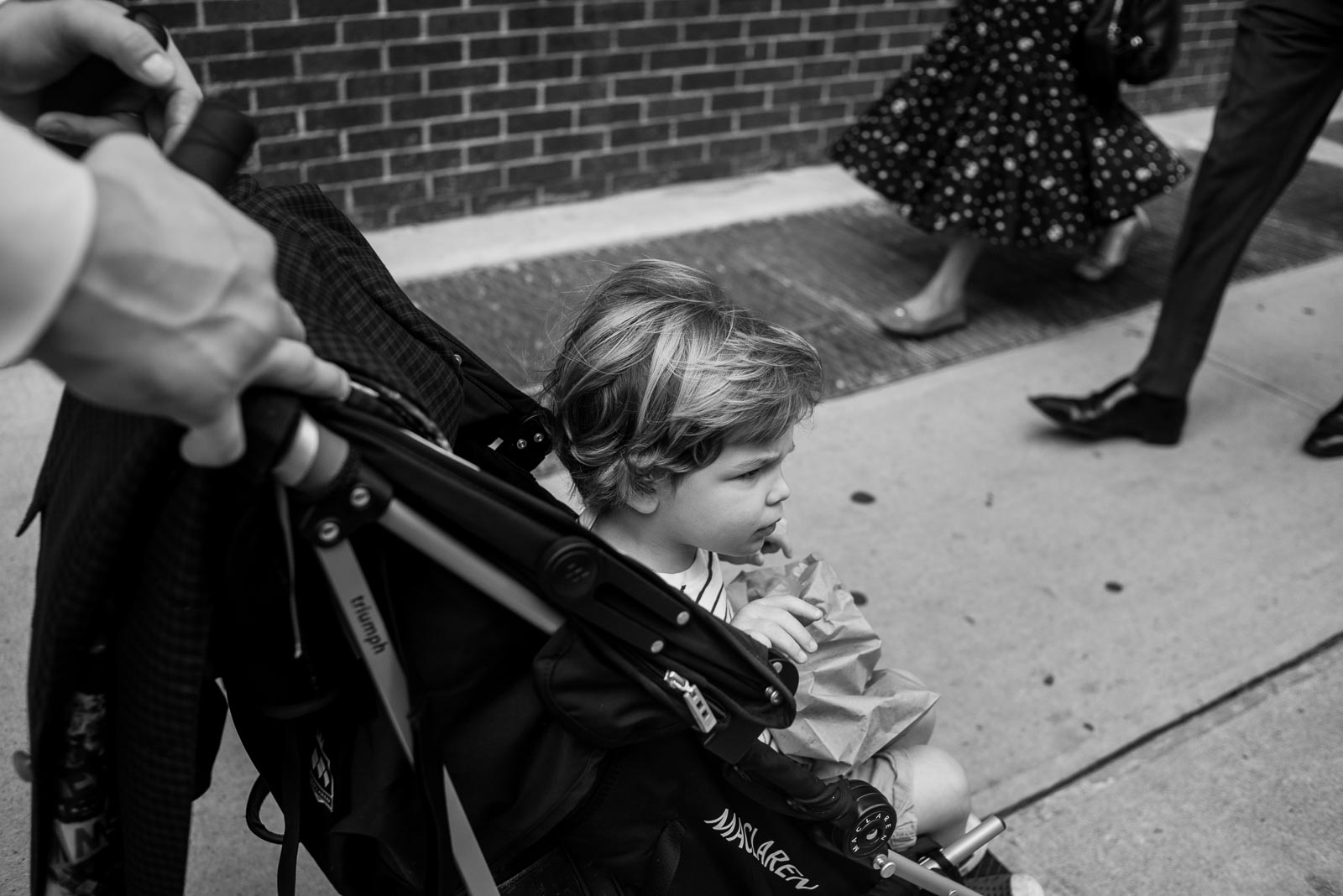 Toddler boy in stroller on new york city sidewalk with couple walking past