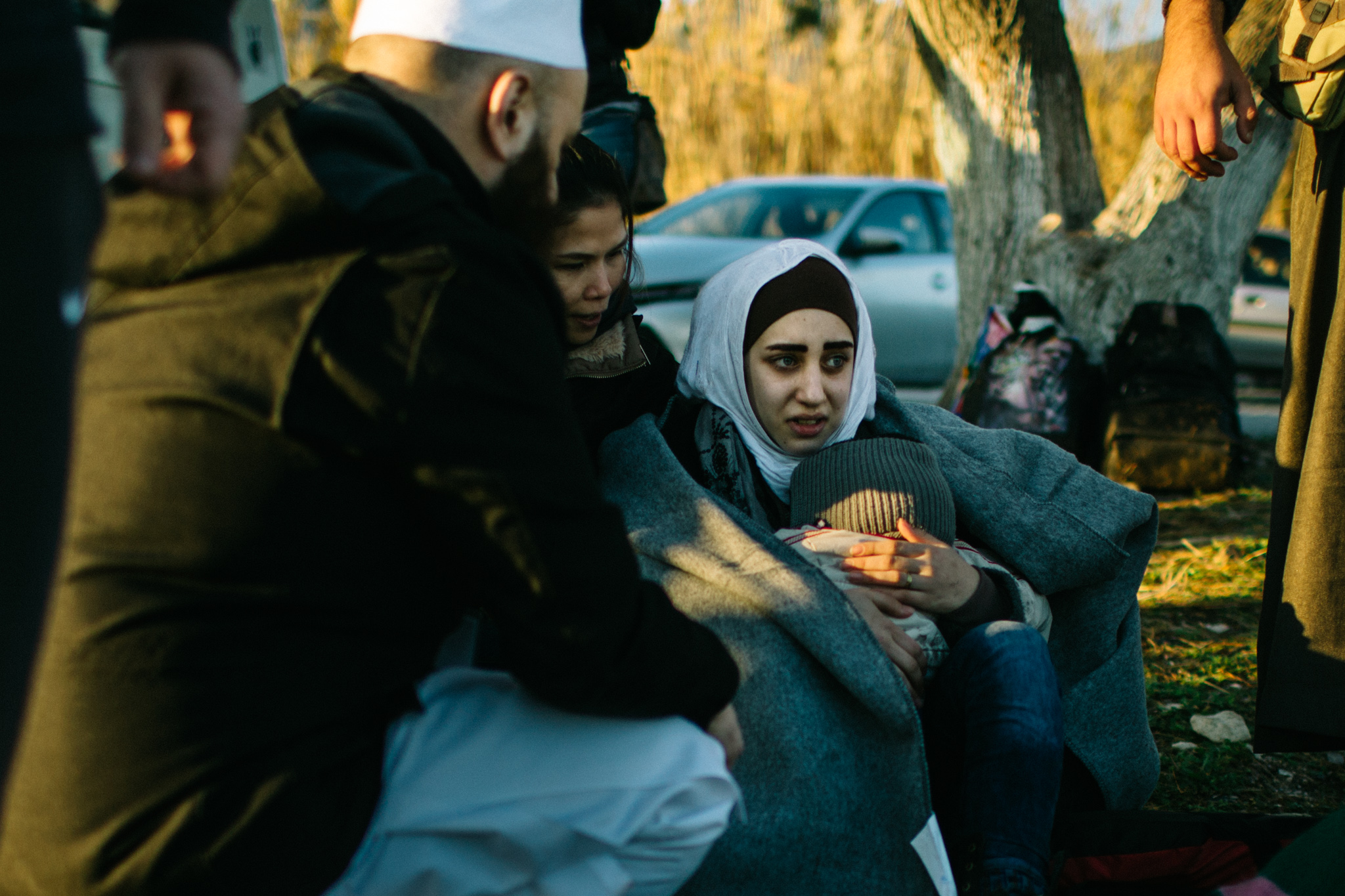A young mother cradles her child on the shores of Lesvos at sunrise.