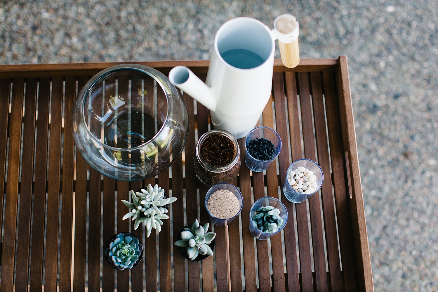 Assemble your supplies. We used a great 8" 100% Recycled Glass Bowl we found at Pat Catans. Three succulents accompanied by unpolished jade stones, pink-white toned rocks & aquarium sand, and a coco coir based potting mix which we pre-moistened along with some activated charcoal carbon.