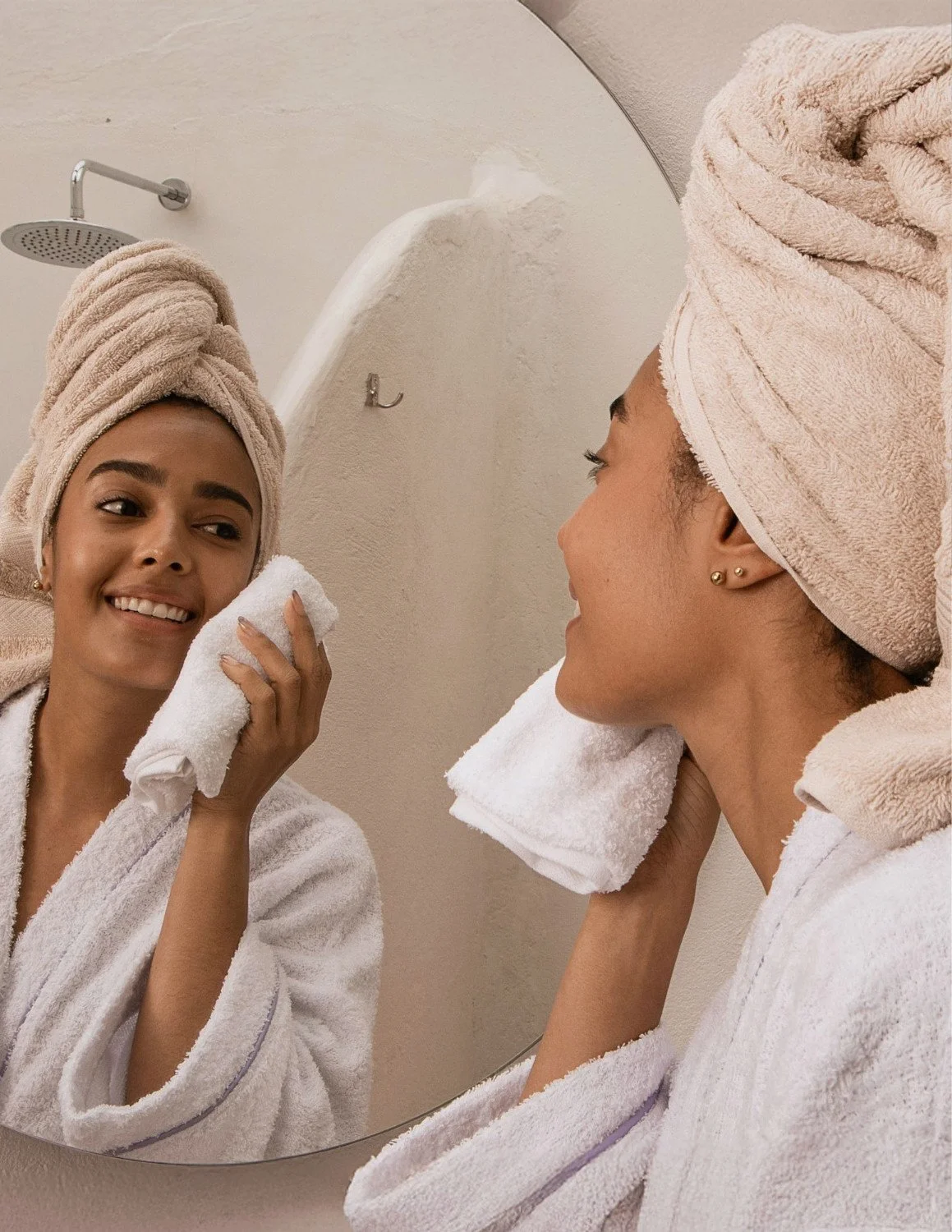 Woman in a robe washing her face in front of a mirror