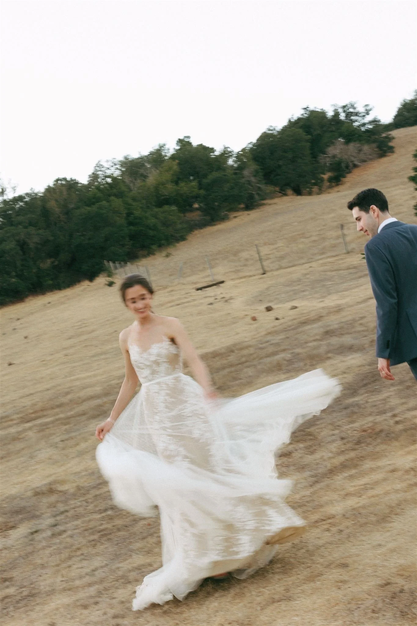 Bride moving in silk wedding dress, soft glamour bridal makeup with luminous skin, outdoor ceremony setting.