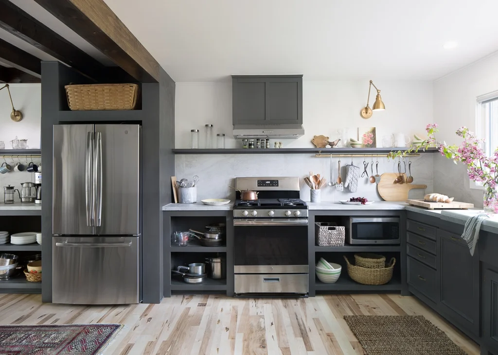 As you can see, the wall is removed — but because we still needed to have a structural beam (and instead of getting an expensive steel beam to expand the space) we keep the beam where it was and created a “box” around the refrig’s new location — clever right! The stove is in the exact same position — again, saving money by not changing the location of the gas or electrical elements. The open shelving cabinets the builder made — more affordable that purchasing cabinets with doors — and the cabinets that do have the drawers — we keep from the old kitchen and painted the same color as the rest of the cabinets — a peppercorn gray. The counter top is 2 x 2 pieces of porcelain tile — not stone — did we fool you? I wanted that old European look with large stone counters and high stone back splash but those tend to be pricey — so I found some tile pieces in a leftover/discount section of a tile shop and the builder put them in and faced them with a piece of wood to make them look thicker — which I then gave a faux stone painted finish too — very easy. Picked up pieces of brass from Signature hardware for two pot racks for around $100 — which really bring this space to another level. The vintage sink I picked up at Mason Brothers architectural salvage yard (we traded some of the cool fixtures that we removed). Almost all of the dishes, bowls, plates, canisters, kitchen utensils I picked up with a few trips to Goodwill. Some of the antique bowls and copper pieces I got at my local antique shop — and all the appliances are new.