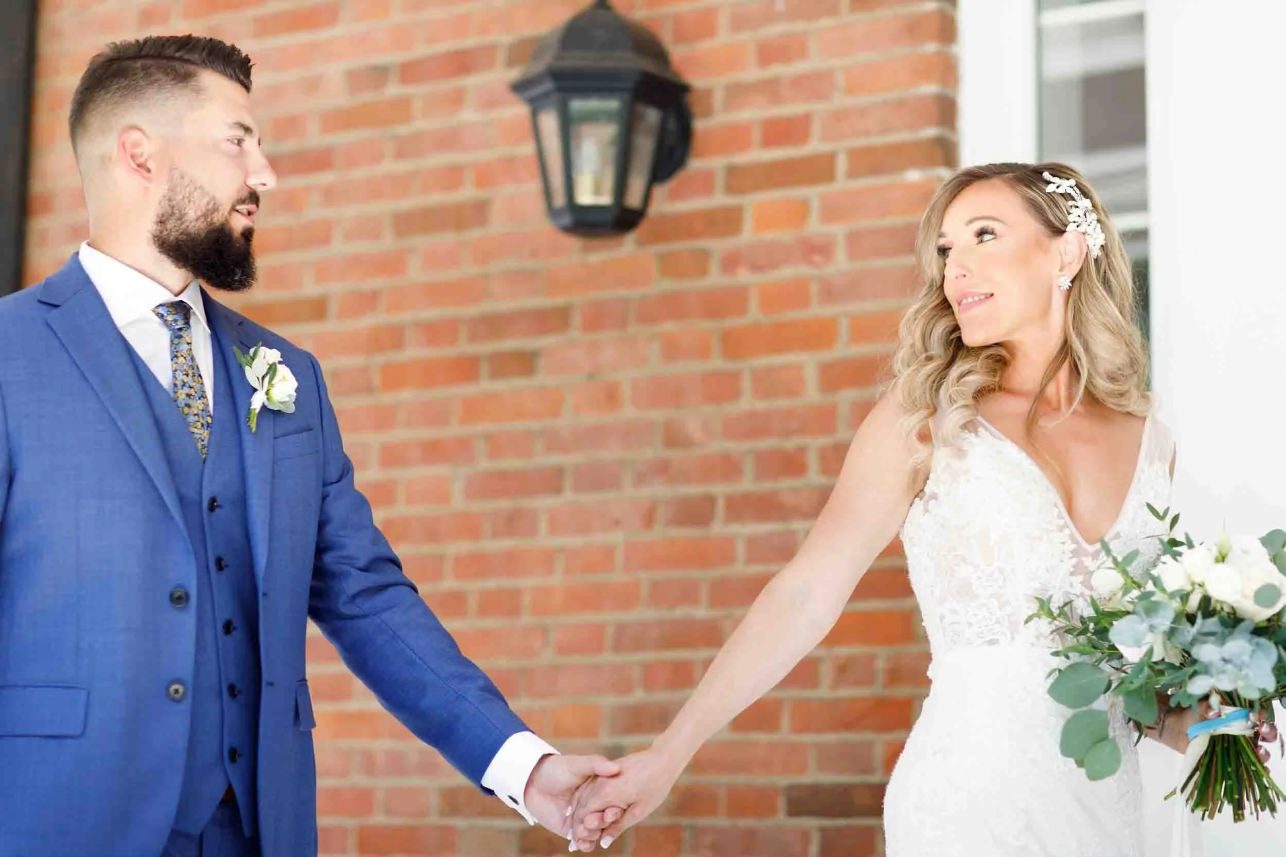 Intimate couple holding hands and walking against historic brick at Gracewood Estate