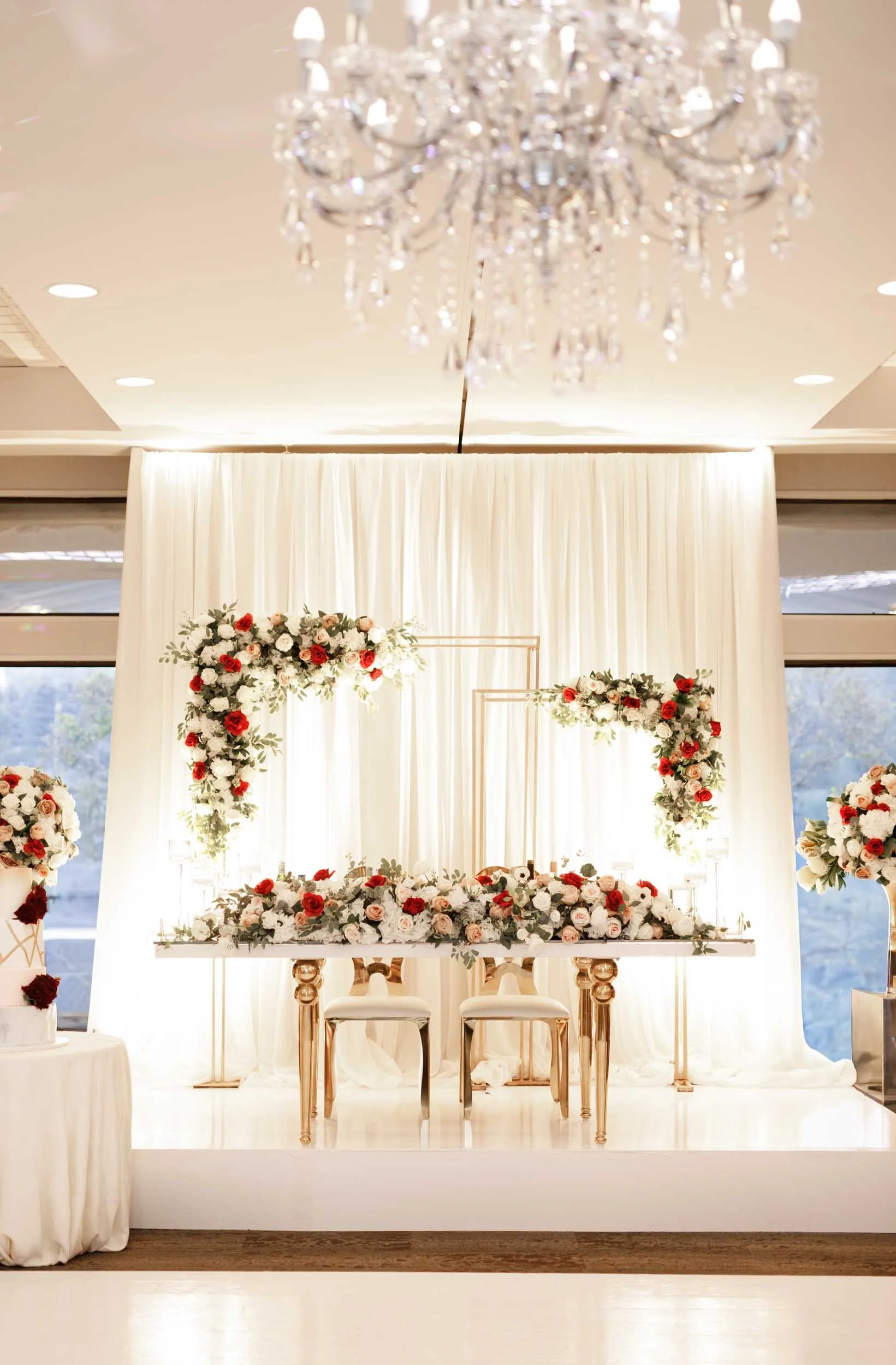 Elegant head table reception backdrop with white drapery and red floral arrangements at The Manor Event Venue in King, Ontario