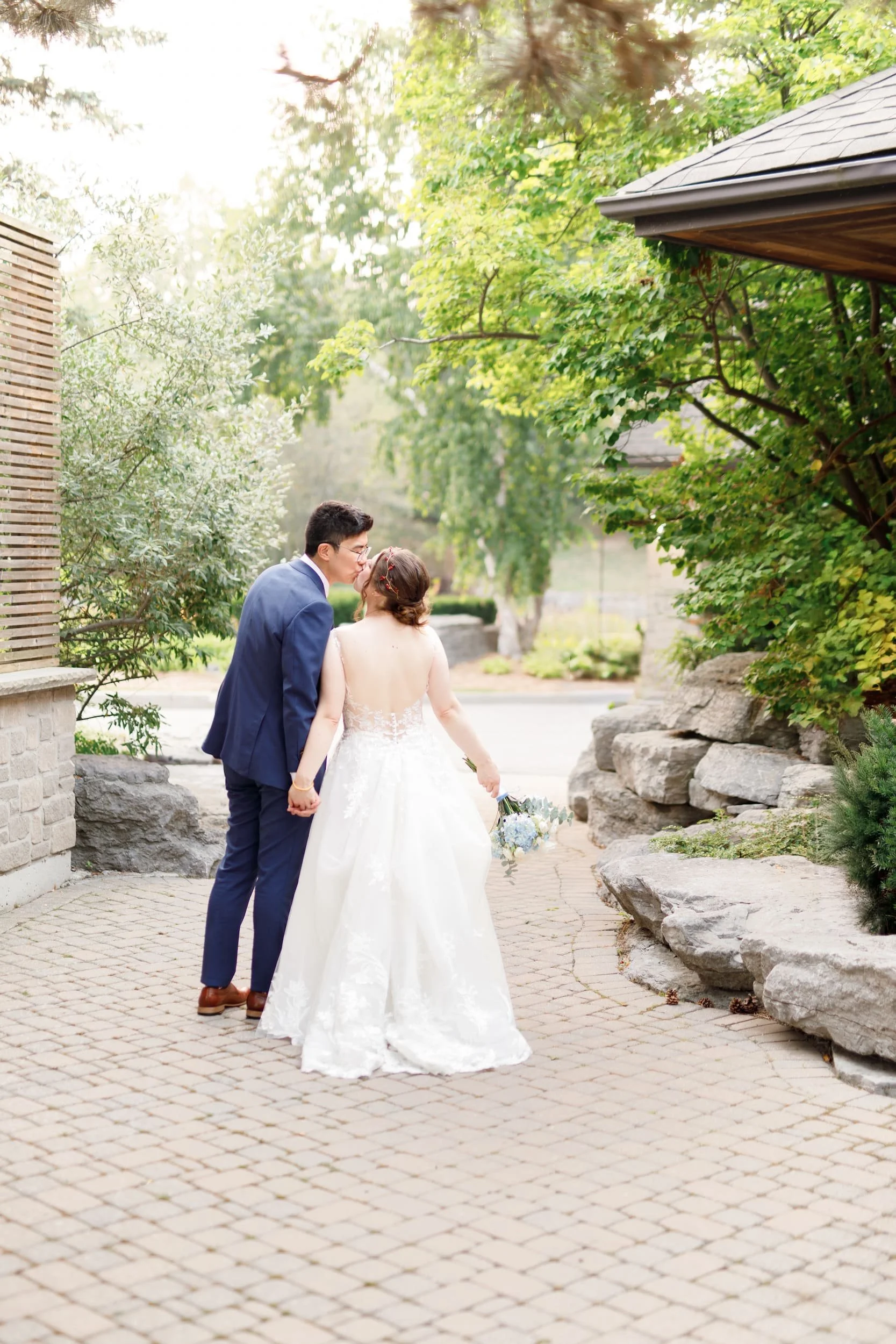 Newlyweds walking hand in hand along stone pathway at The Manor Event Venue in King, Ontario