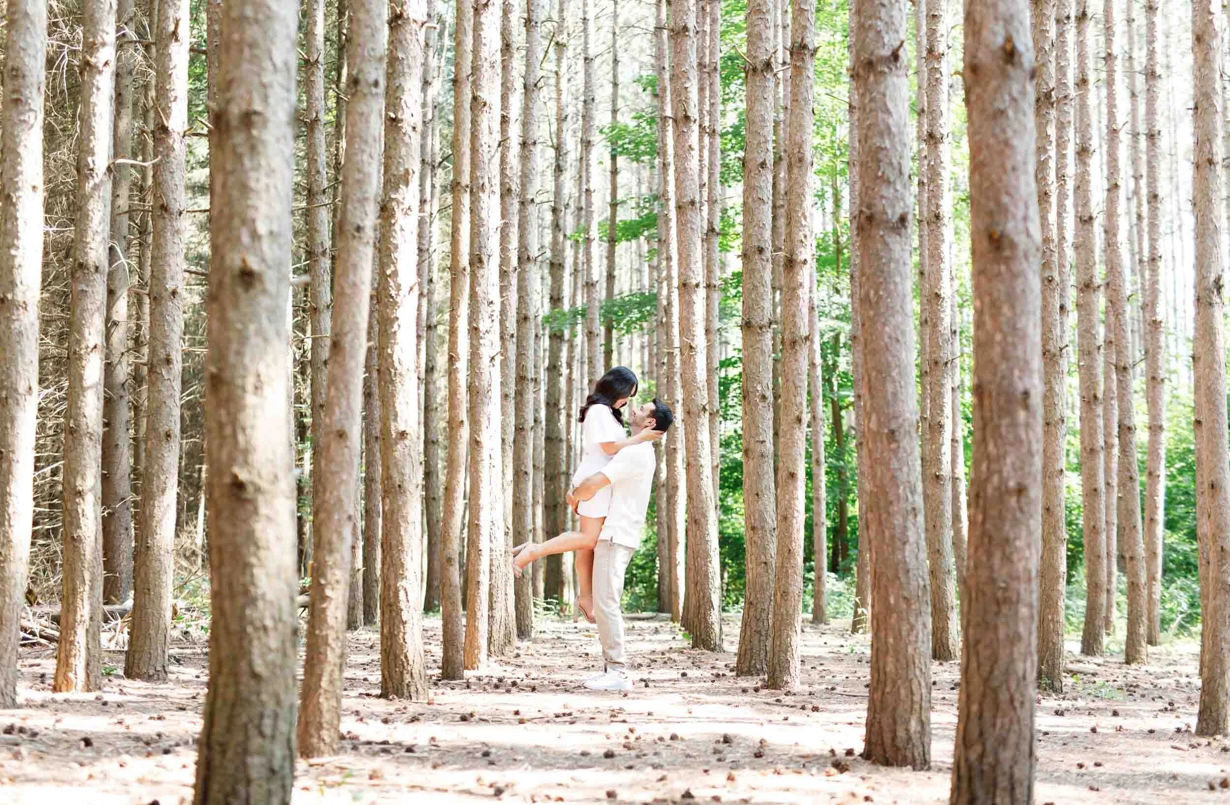 Groom lifting his fiancée in a joyful moment among the tall trees at Kortright Centre for Conservation in Woodbridge Ontario