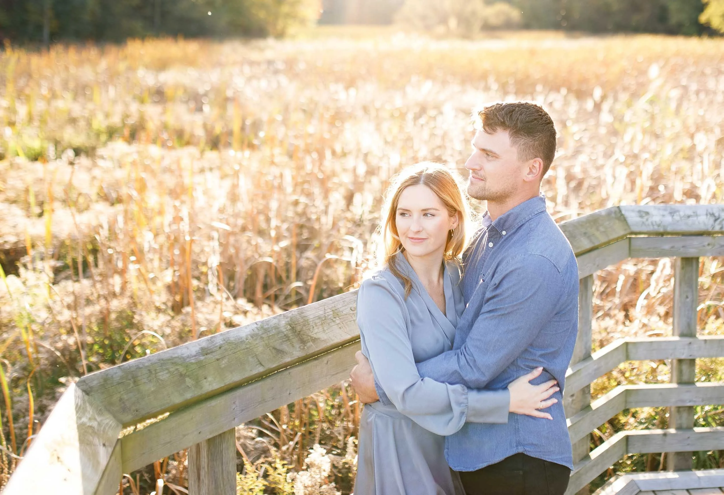Engaged couple standing together on the boardwalk overlooking the marsh at Grindstone Marsh Trail in Burlington