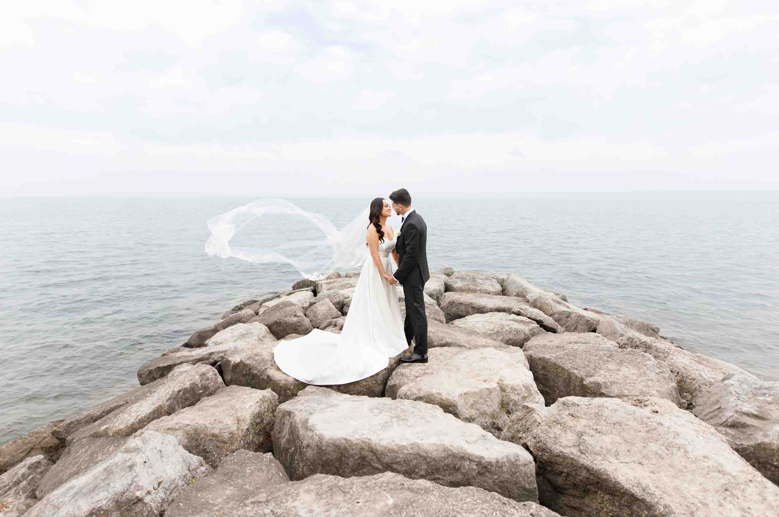 Bride and groom standing on the lakeside rocks at the Pearle Hotel in Burlington