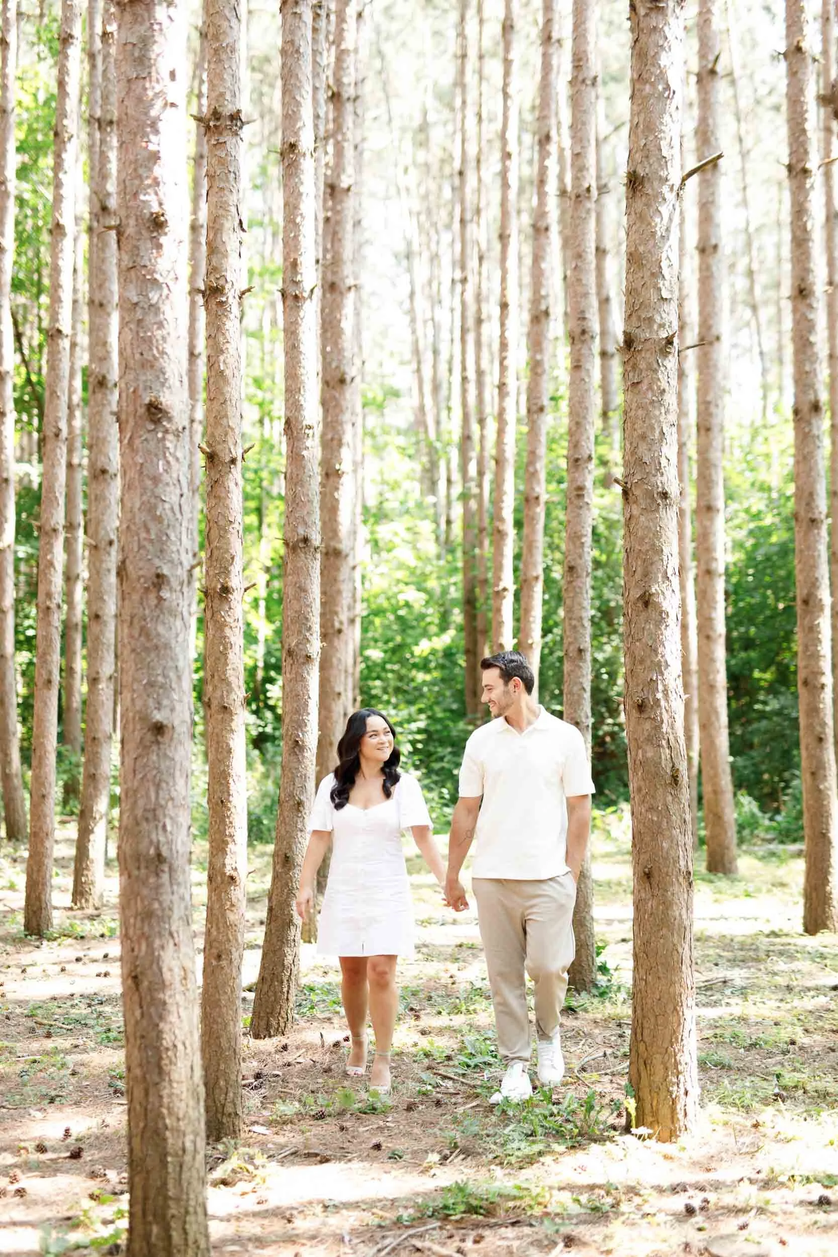 Couple smiling at each other in the forest during engagement photos at Kortright Centre in Woodbridge, Ontario