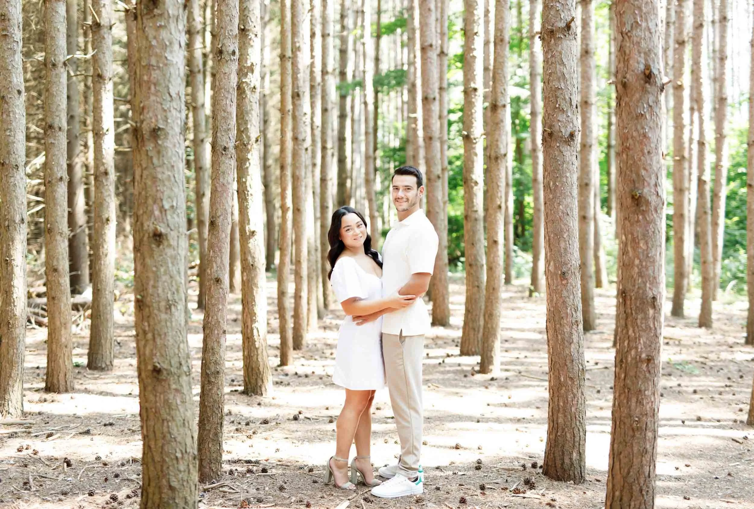 Couple embracing between trees during engagement photos at Kortright Centre for Conservation in Woodbridge, Ontario