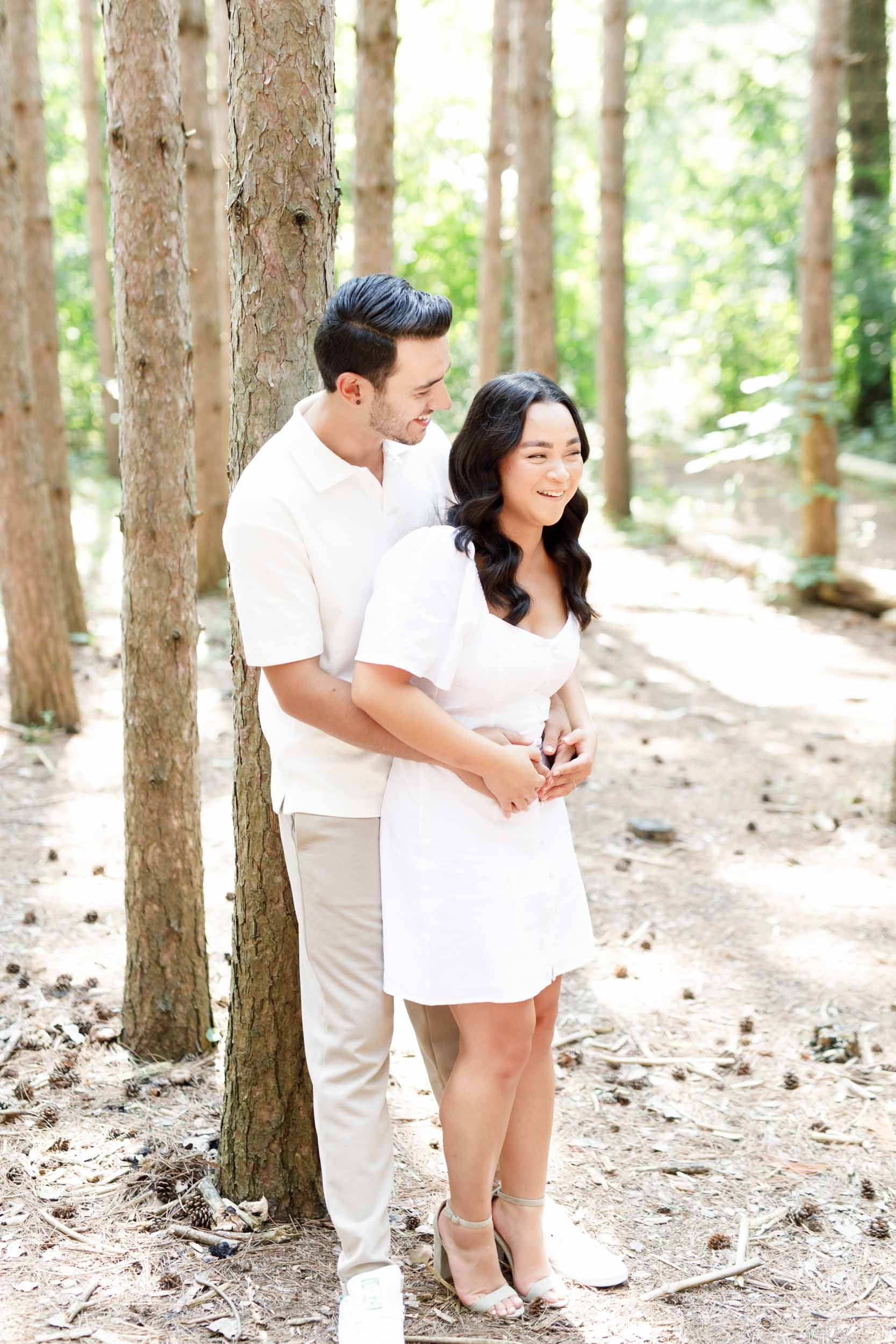 Couple standing close together between trees at Kortright Centre for Conservation in Woodbridge, Ontario