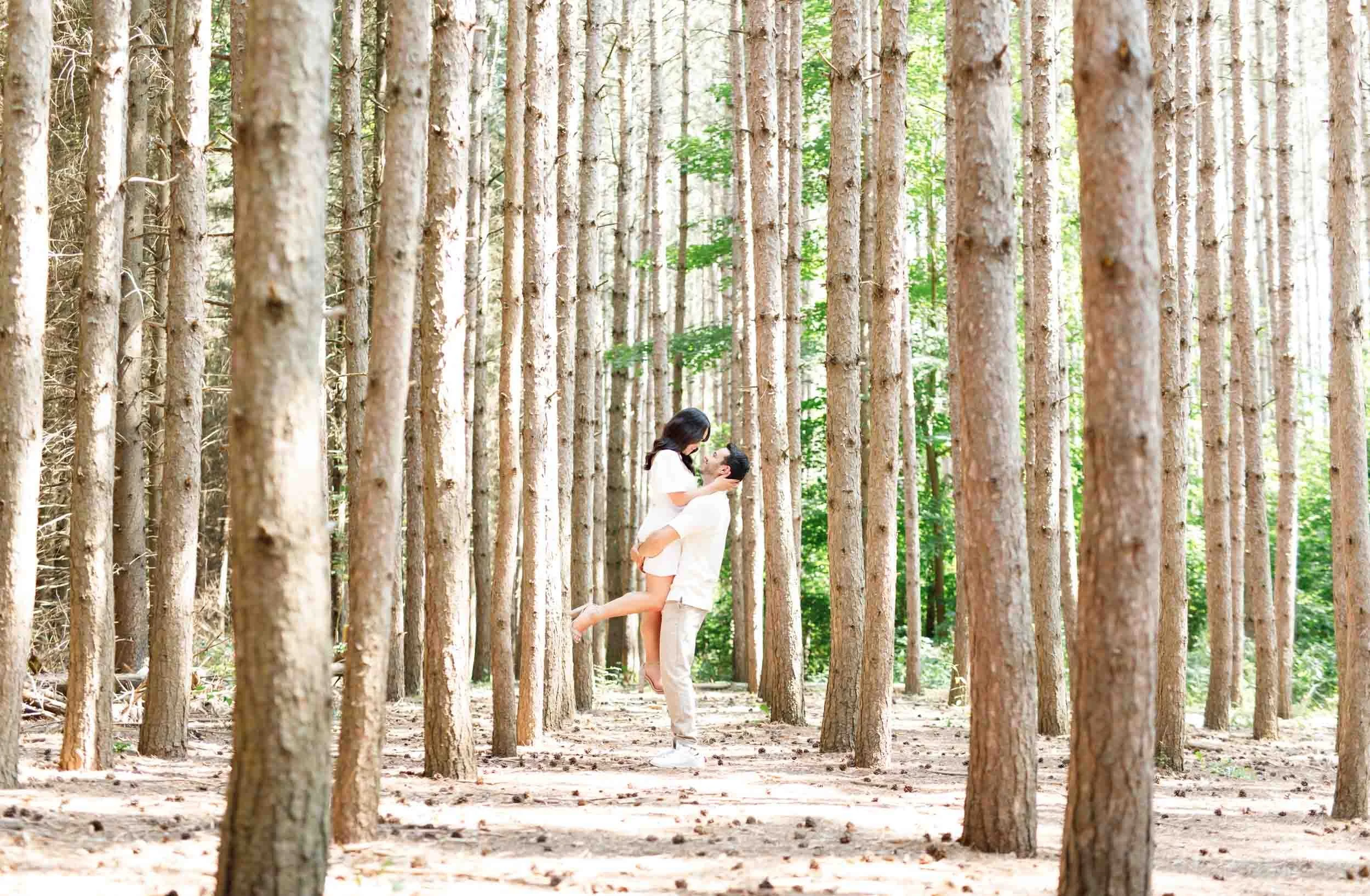 Couple standing together among pine trees during engagement photos at Kortright Centre in Woodbridge, Ontario