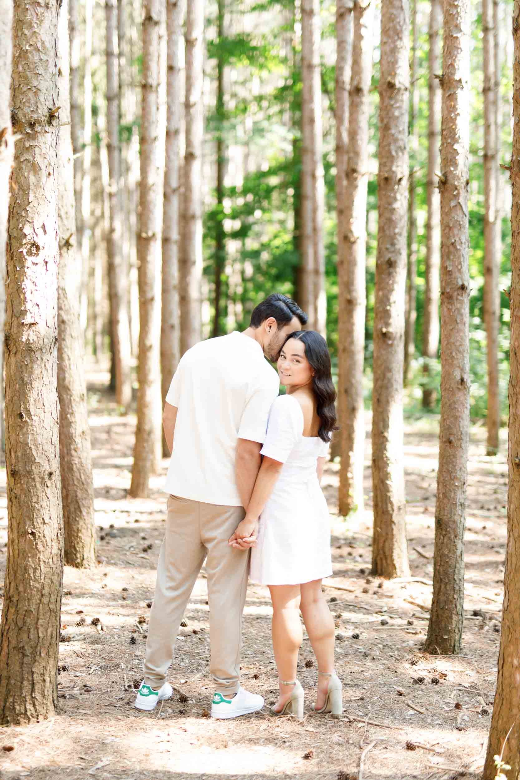 Couple standing close between trees during engagement photos at Kortright Centre for Conservation in Woodbridge, Ontario