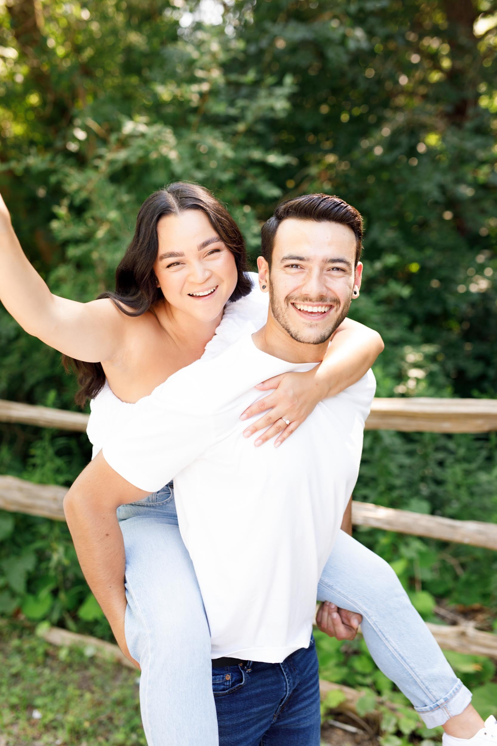 Bride waving while riding on groom’s back at Kortright Centre in Woodbridge, Ontario