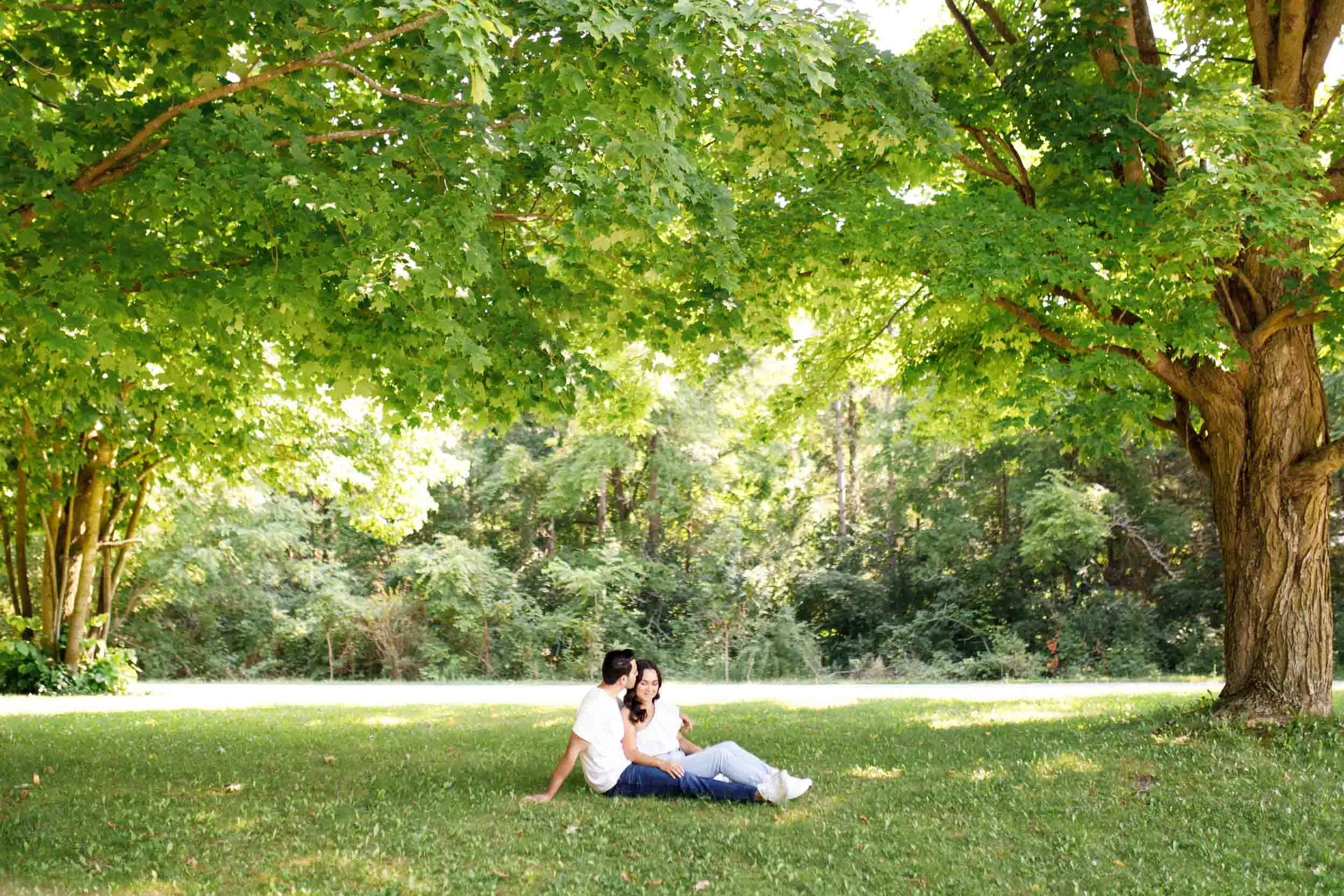 Wide shot of couple sitting on grass during Kortright Centre engagement in Woodbridge, Ontario