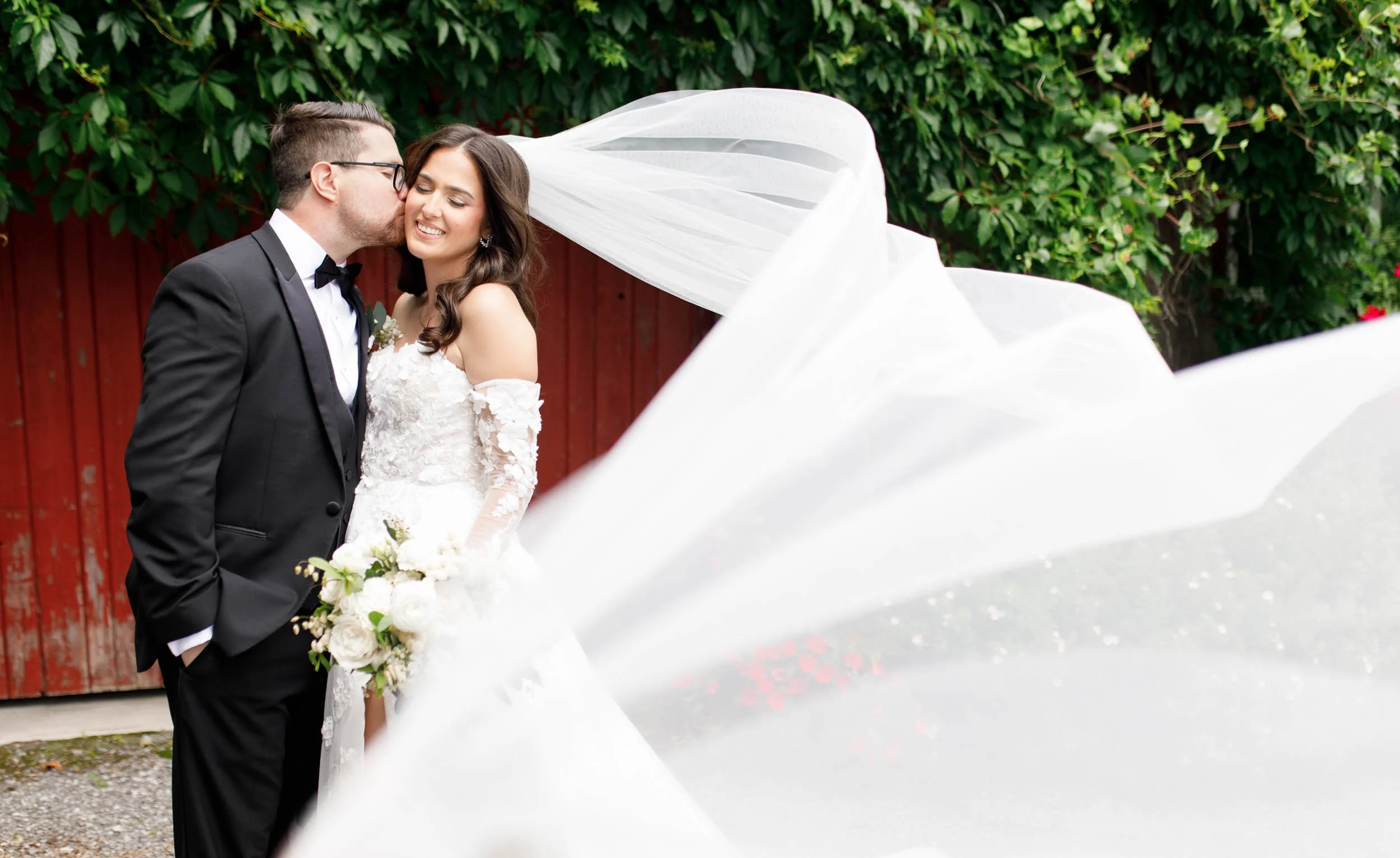 Bride and groom kissing in front of rustic barn during portraits at Cambium Farms in Alton, Ontario