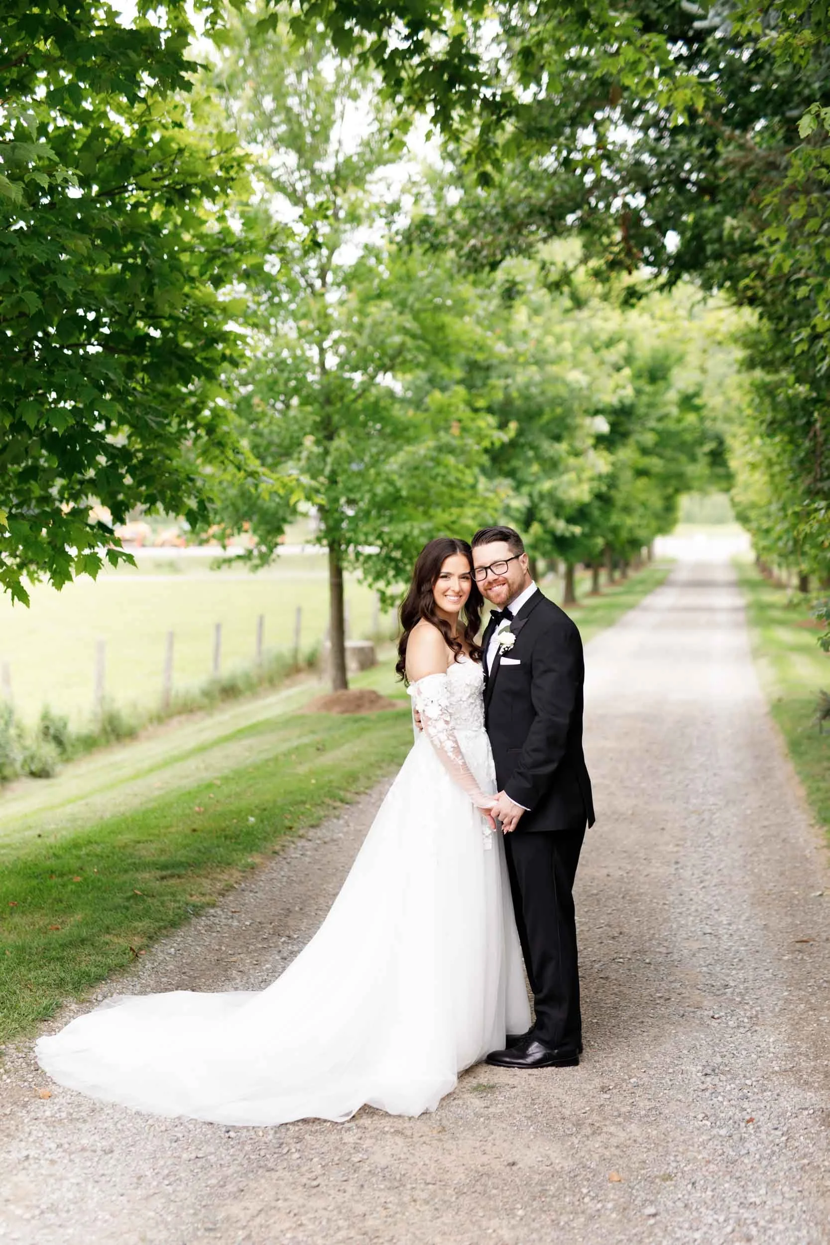 Bride and groom standing together on the tree-lined driveway at Cambium Farms in Alton, Ontario