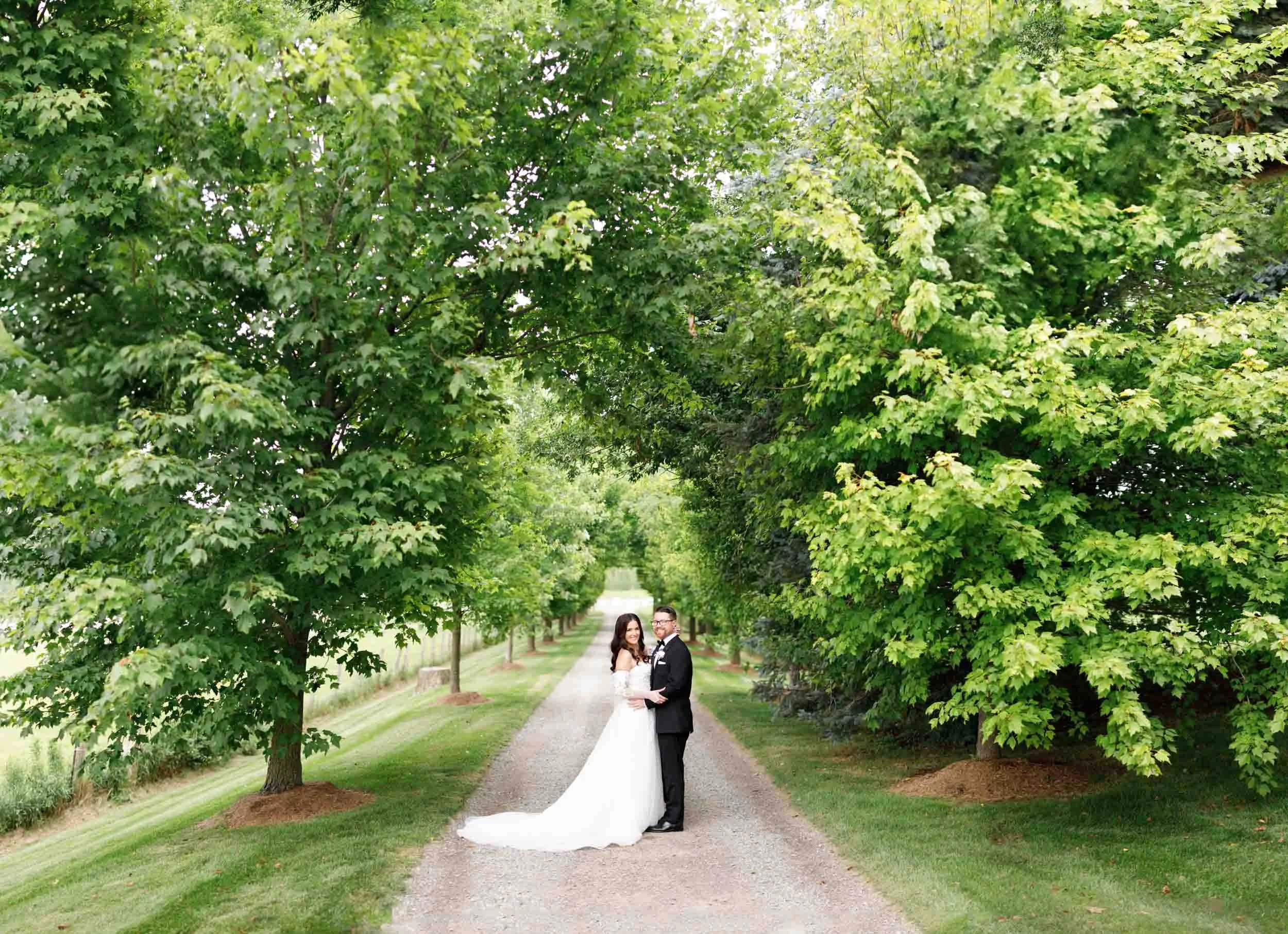 Wide shot of bride and groom walking beneath trees at a Cambium Farms wedding in Alton, Ontario