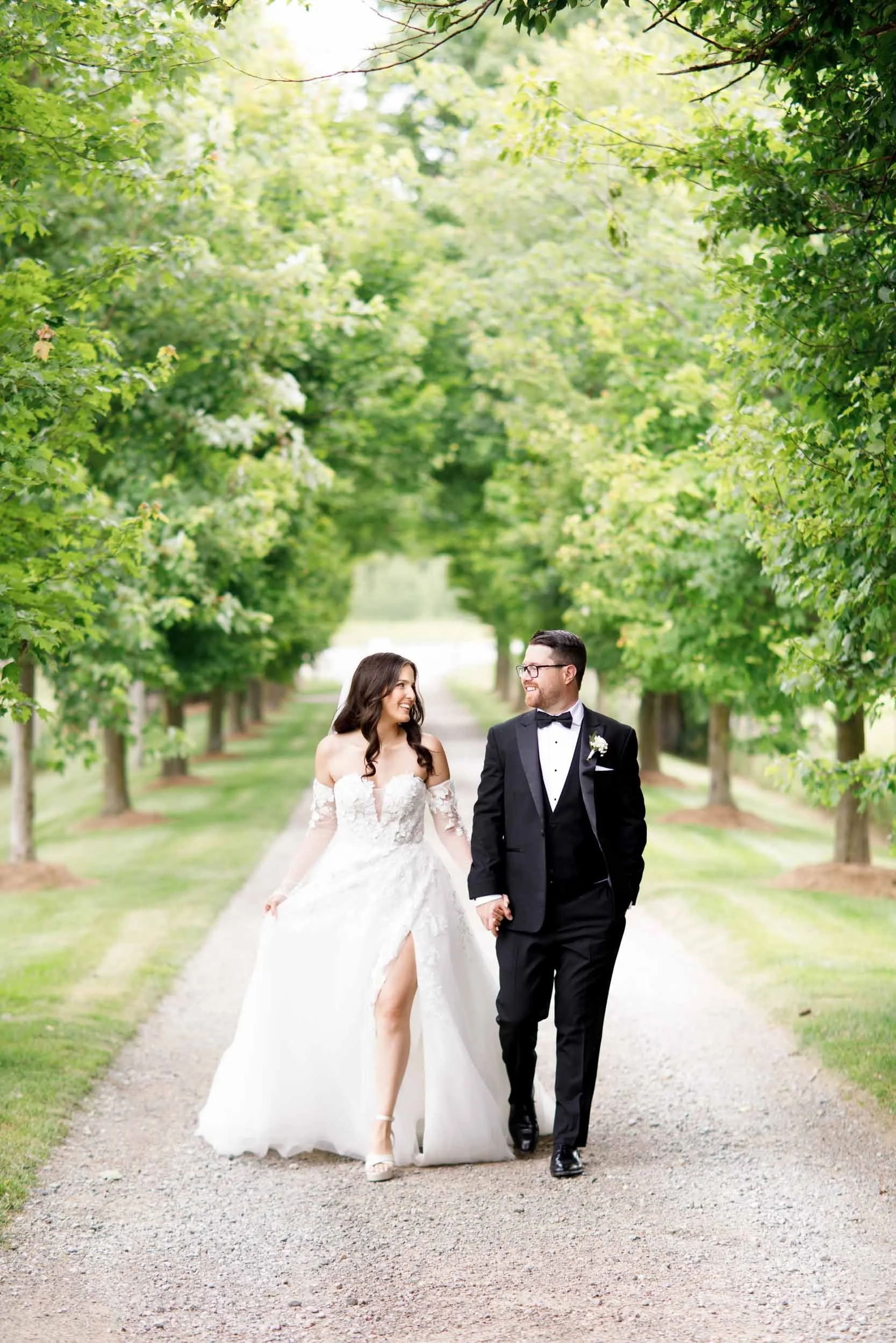 Bride and groom walking away together on the Cambium Farms tree-lined driveway in Alton, Ontario
