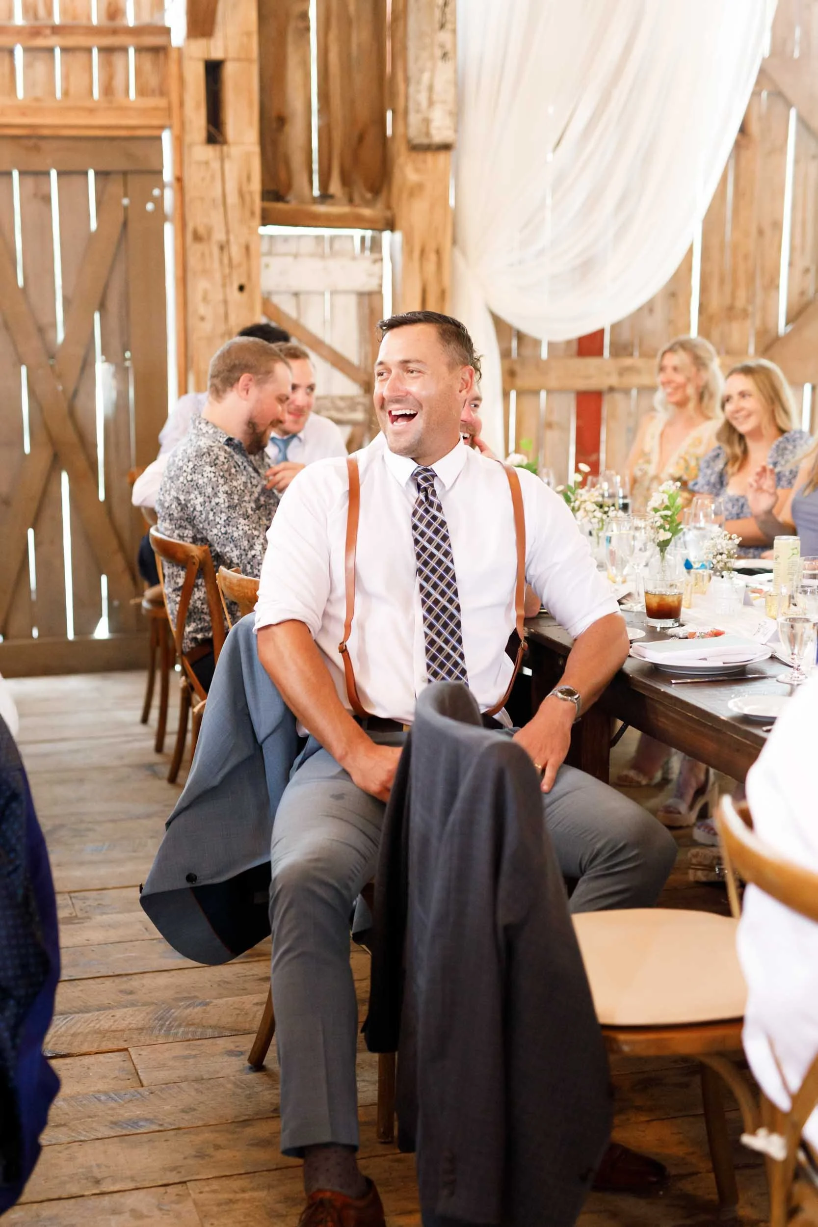 Wedding guest laughing during speeches inside the Cambium Farms barn in Alton, Ontario