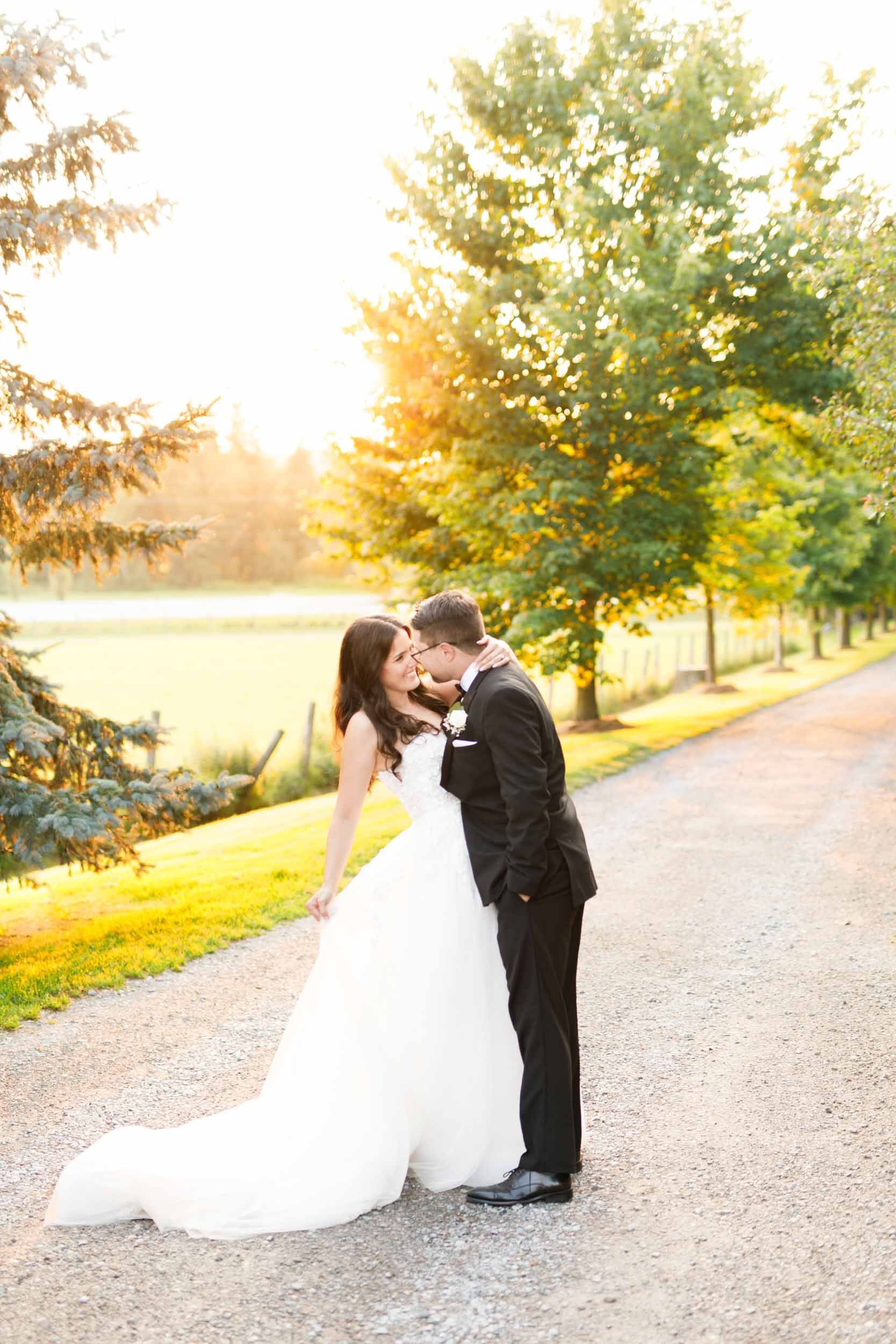 Bride and groom sharing a kiss on the Cambium Farms driveway at sunset in Alton, Ontario