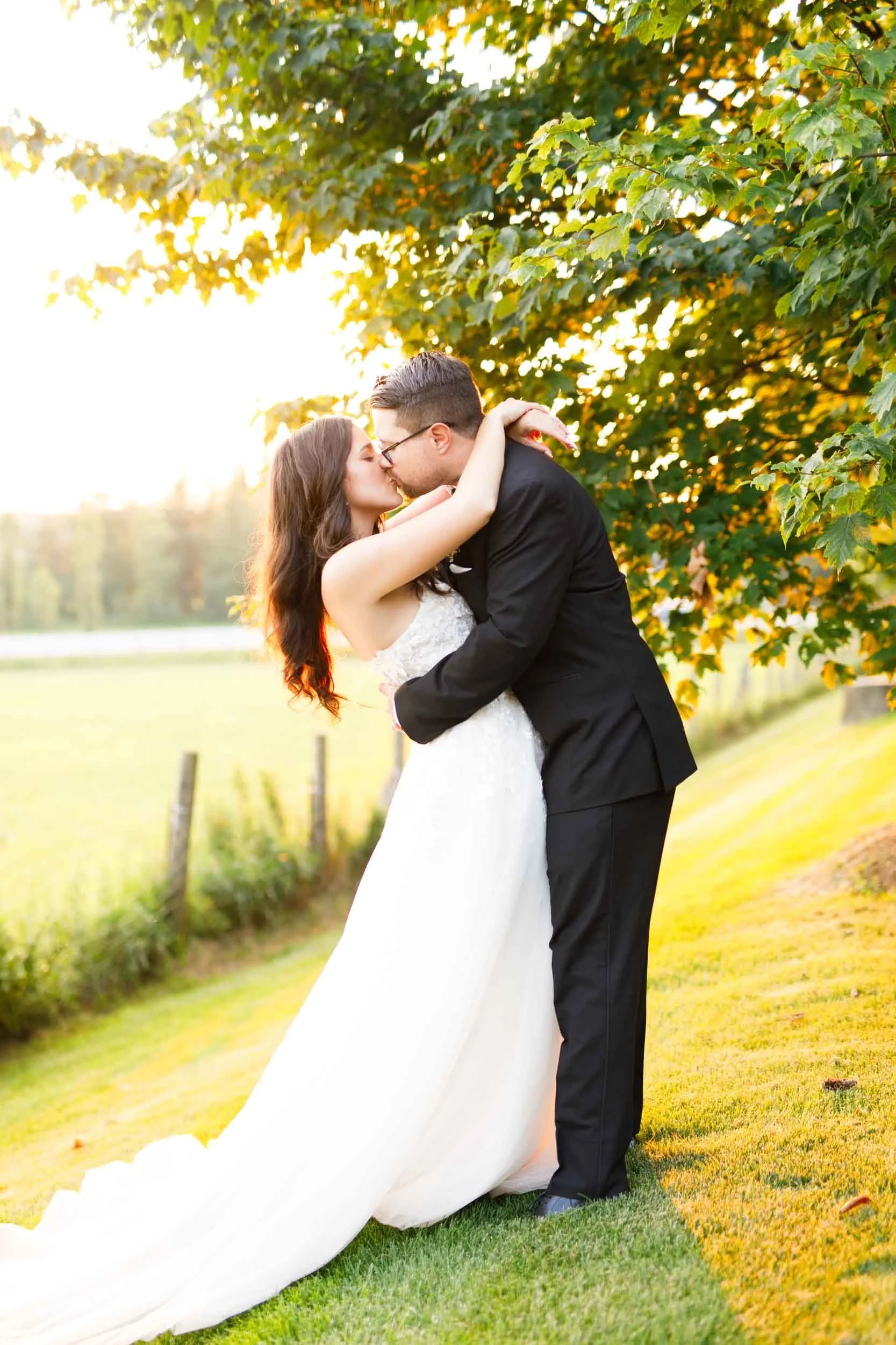 Bride and groom kissing at sunset beneath trees at a Cambium Farms wedding in Alton, Ontario