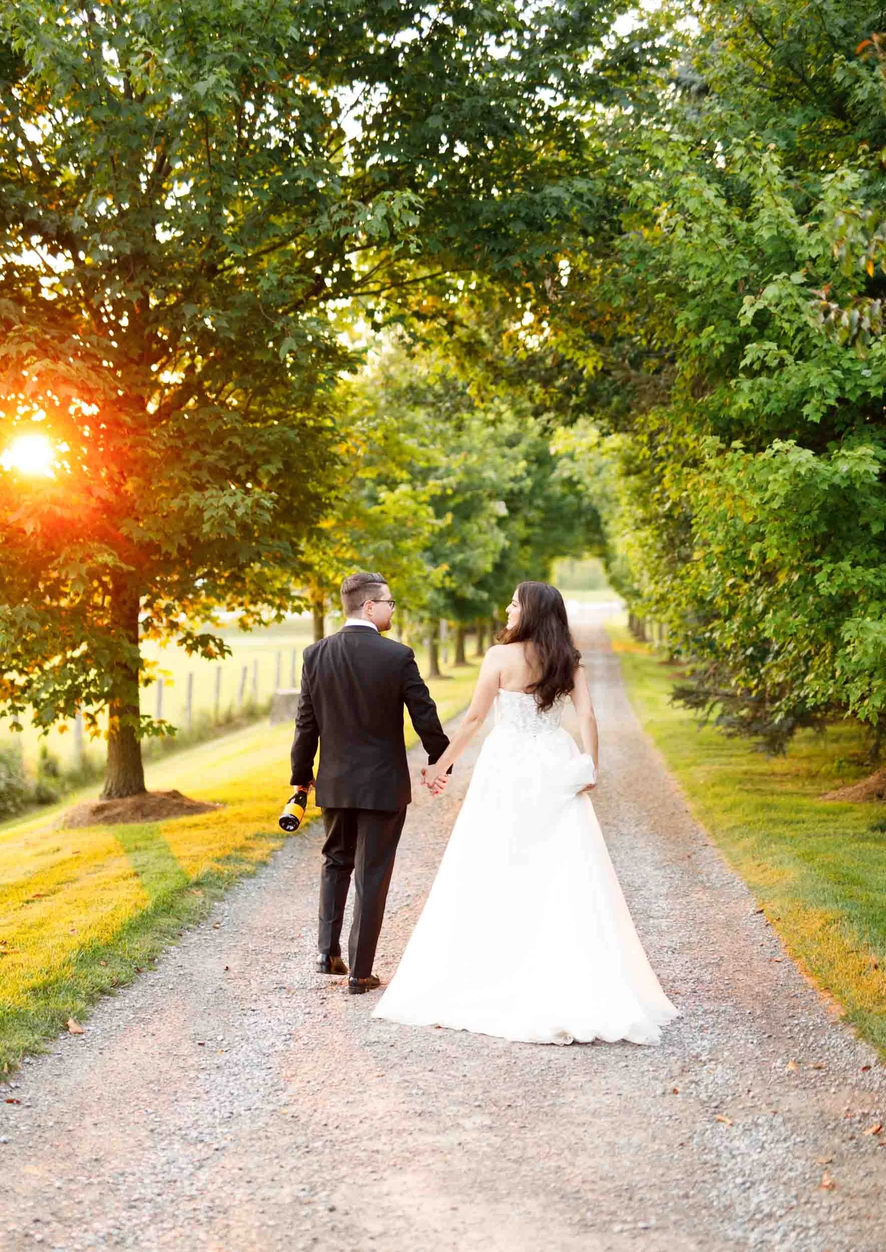 Bride and groom walking away together on the tree-lined driveway at Cambium Farms in Alton, Ontario