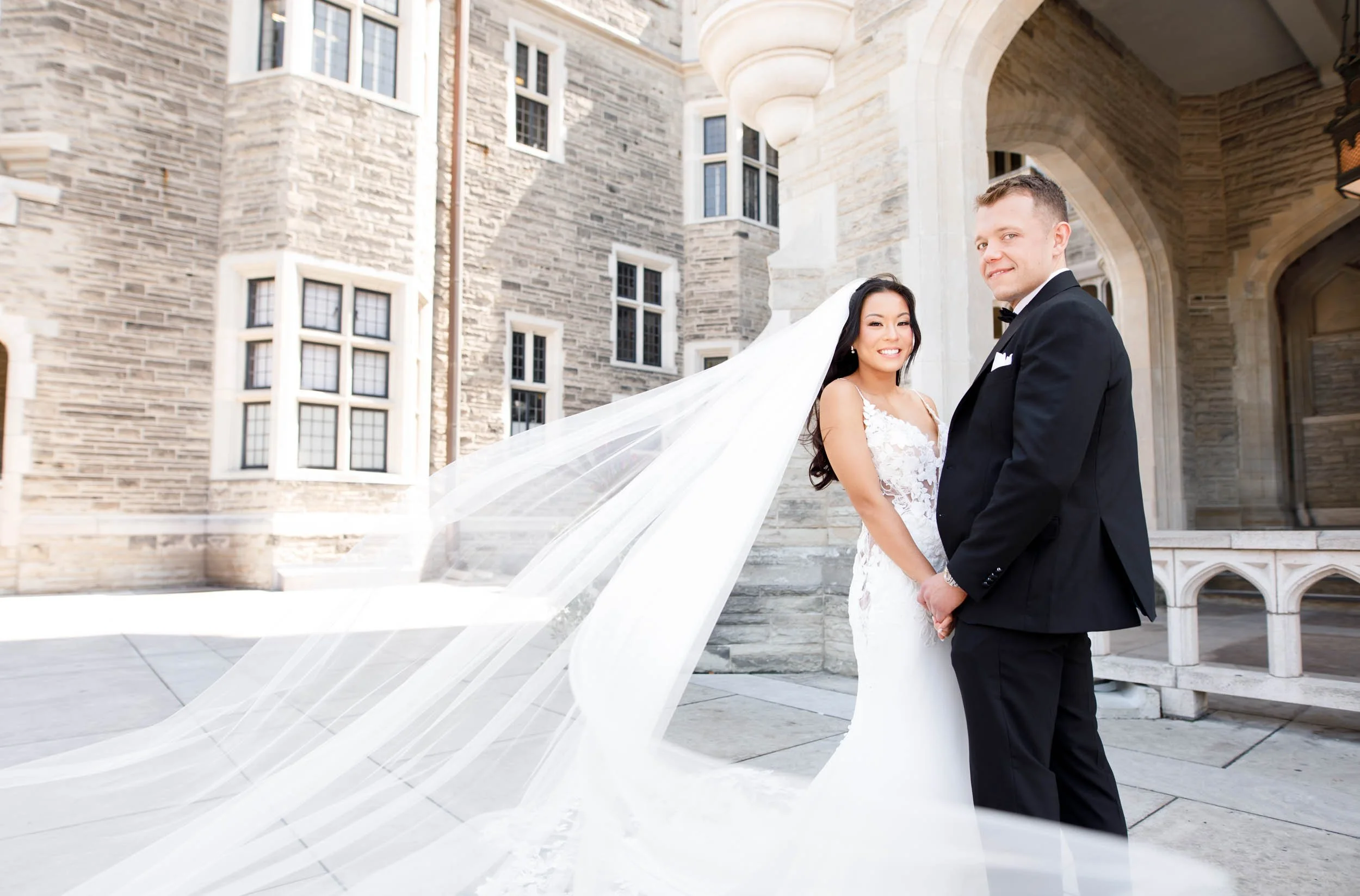 Bride and groom posing with a long flowing veil at Casa Loma in Toronto