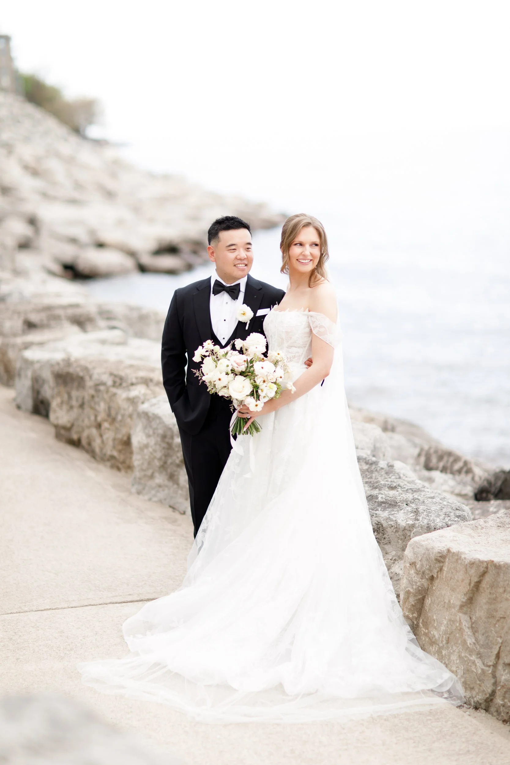 Bride and groom standing on the rocky shoreline at the Pearle Hotel in Burlington Ontario