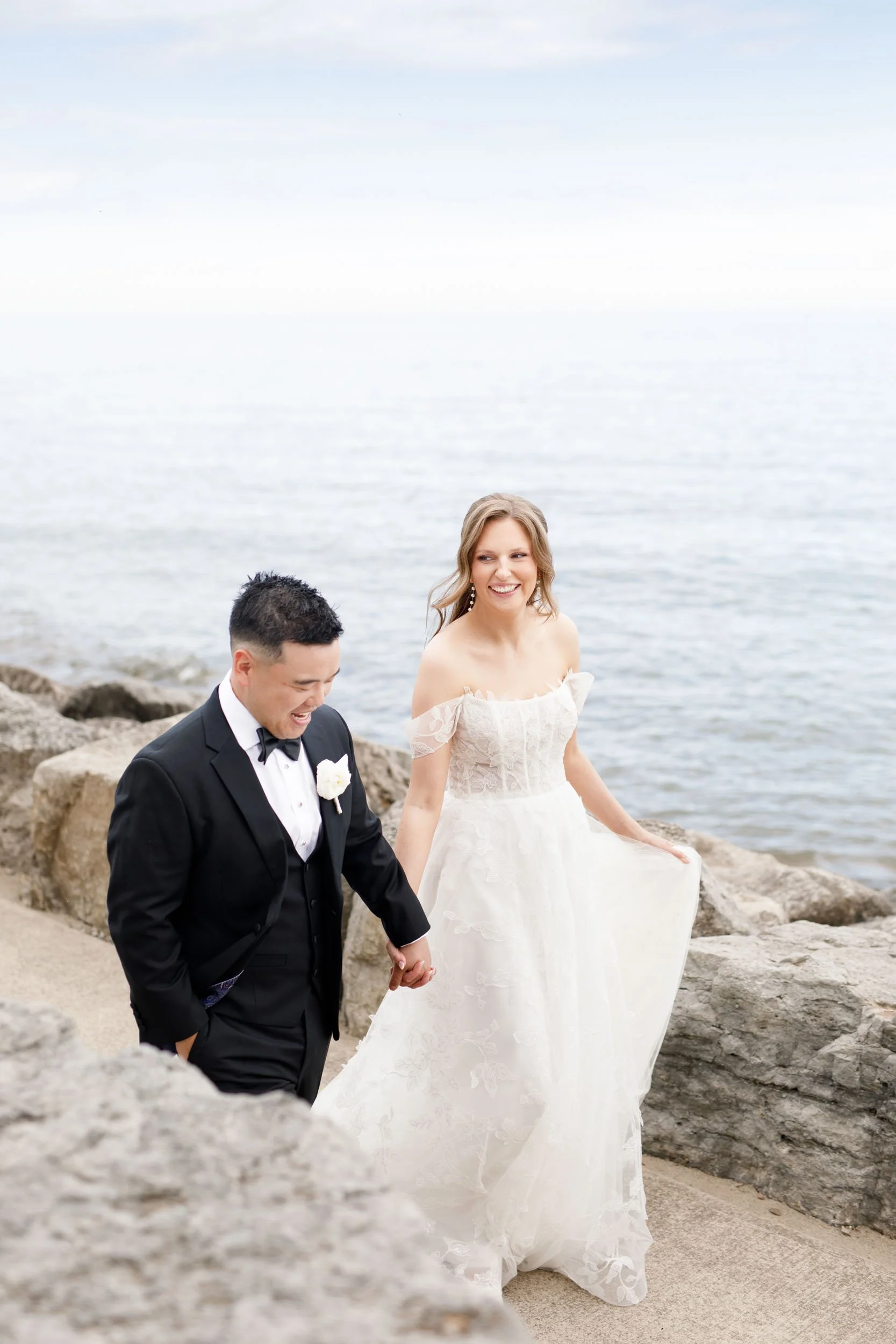 Bride and groom walking along the waterfront rocks at the Pearle Hotel in Burlington Ontario