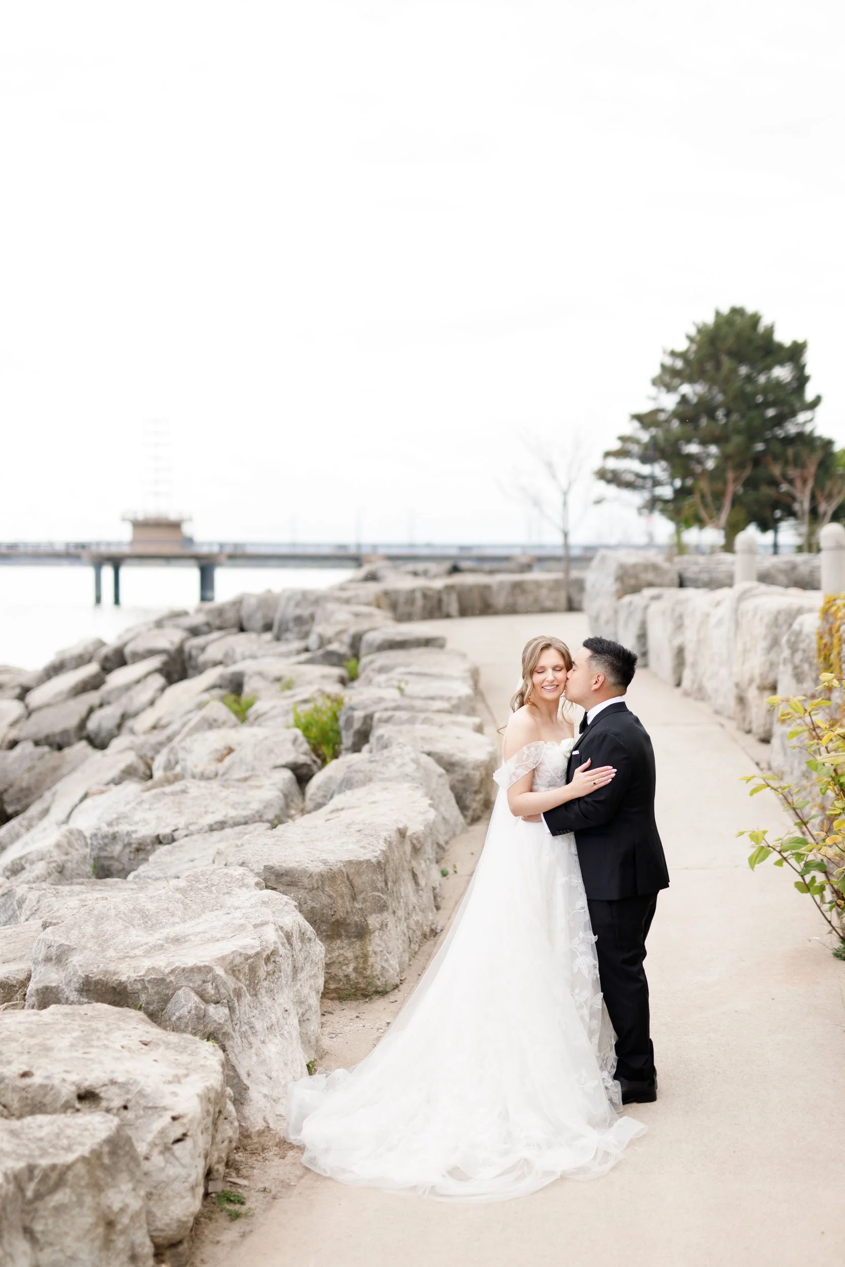Wide view of the bride and groom on the waterfront rocks at the Pearle Hotel in Burlington Ontario