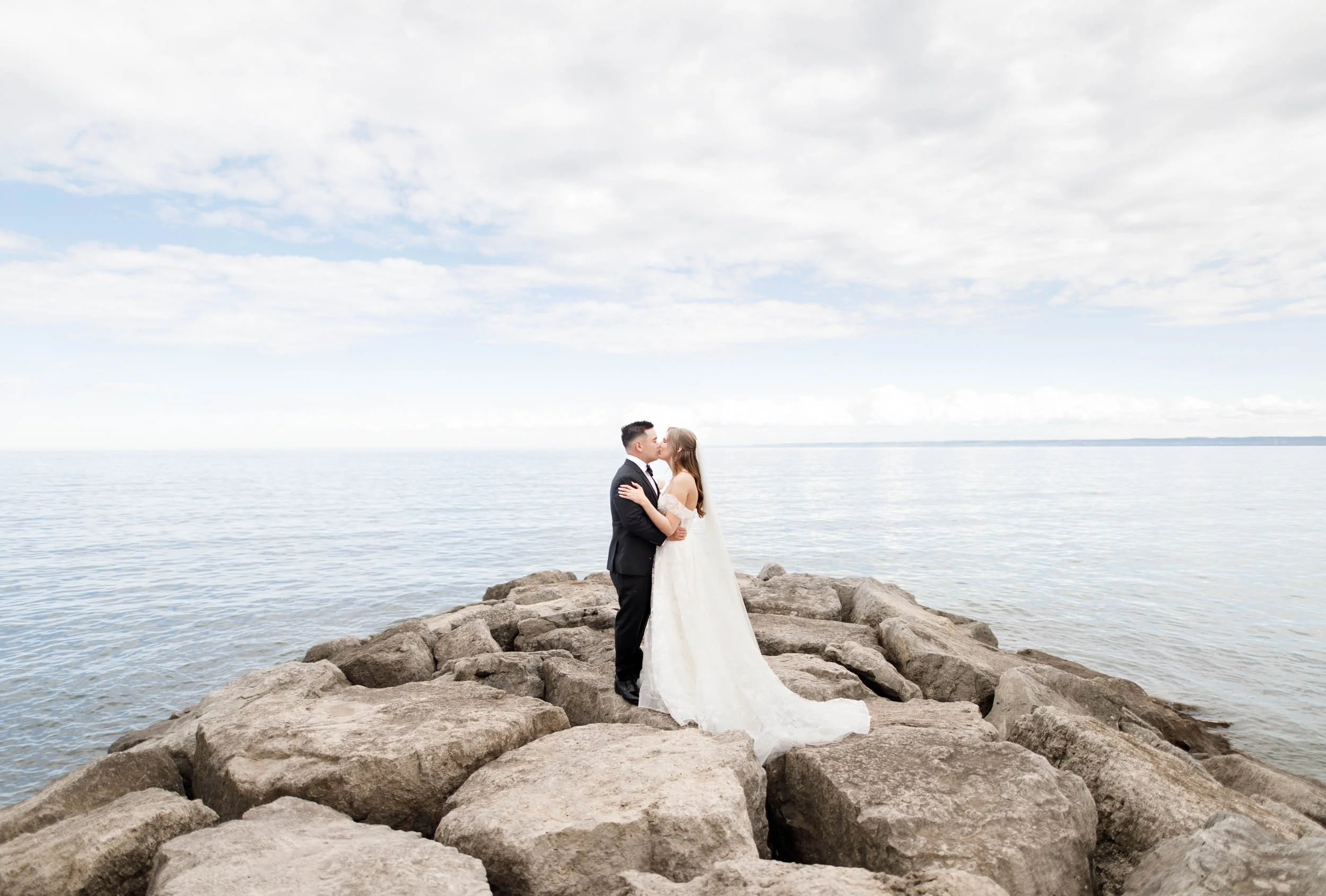 Bride and groom kissing on the rocks by the lake at the Pearle Hotel in Burlington Ontario