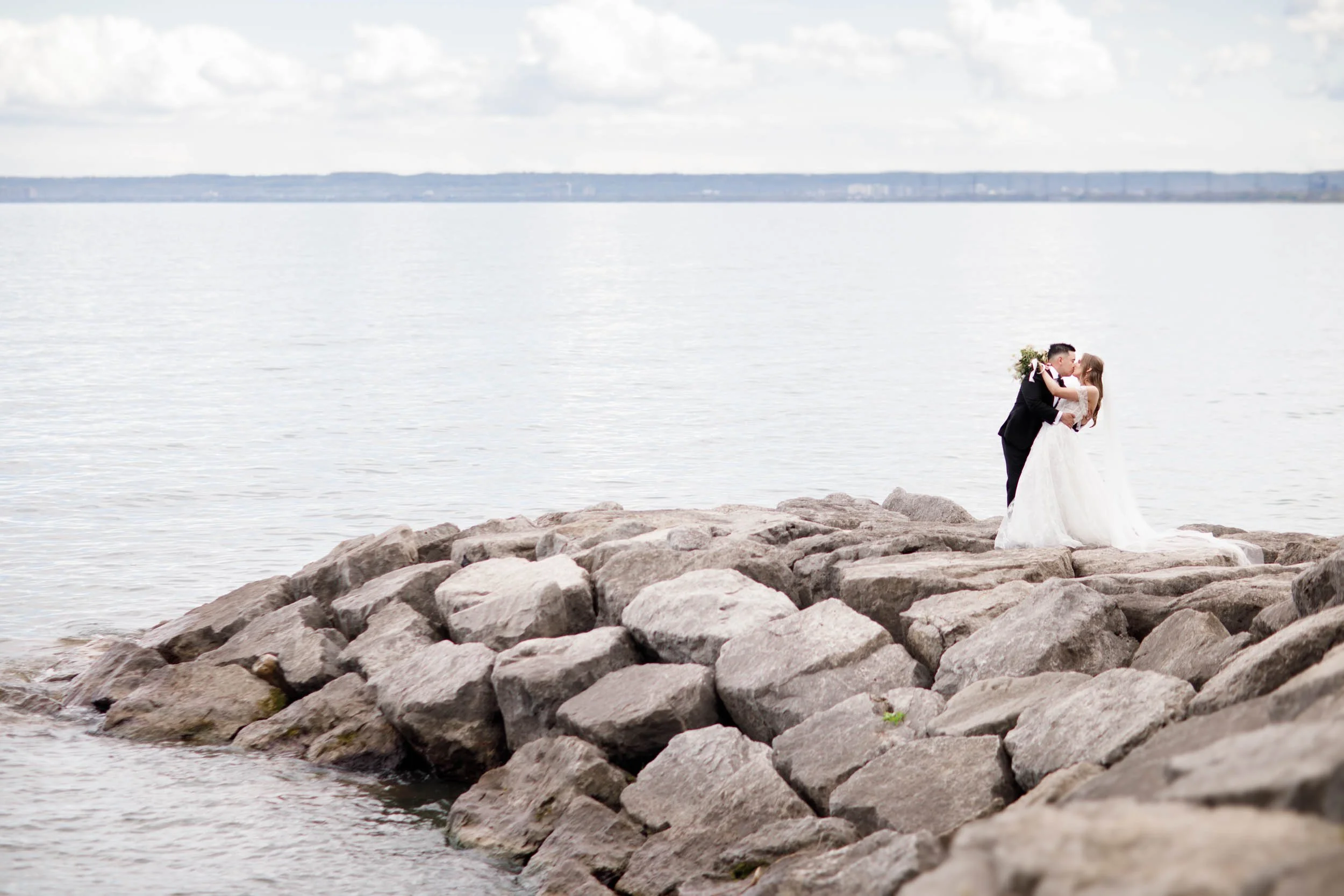 Bride and groom posing on the rocky waterfront at the Pearle Hotel in Burlington Ontario