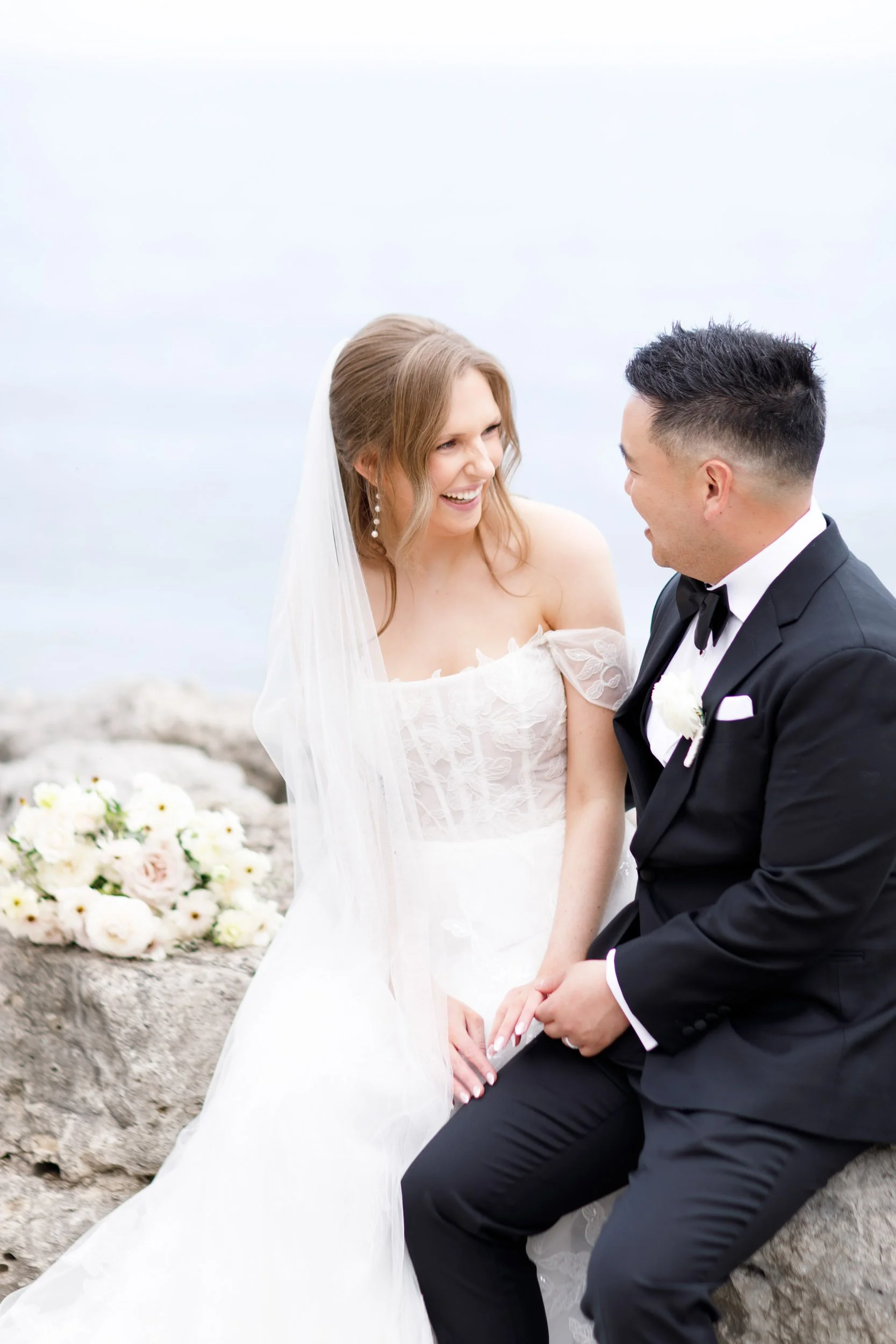 Bride and groom smiling at each other on the waterfront rocks at the Pearle Hotel in Burlington Ontario