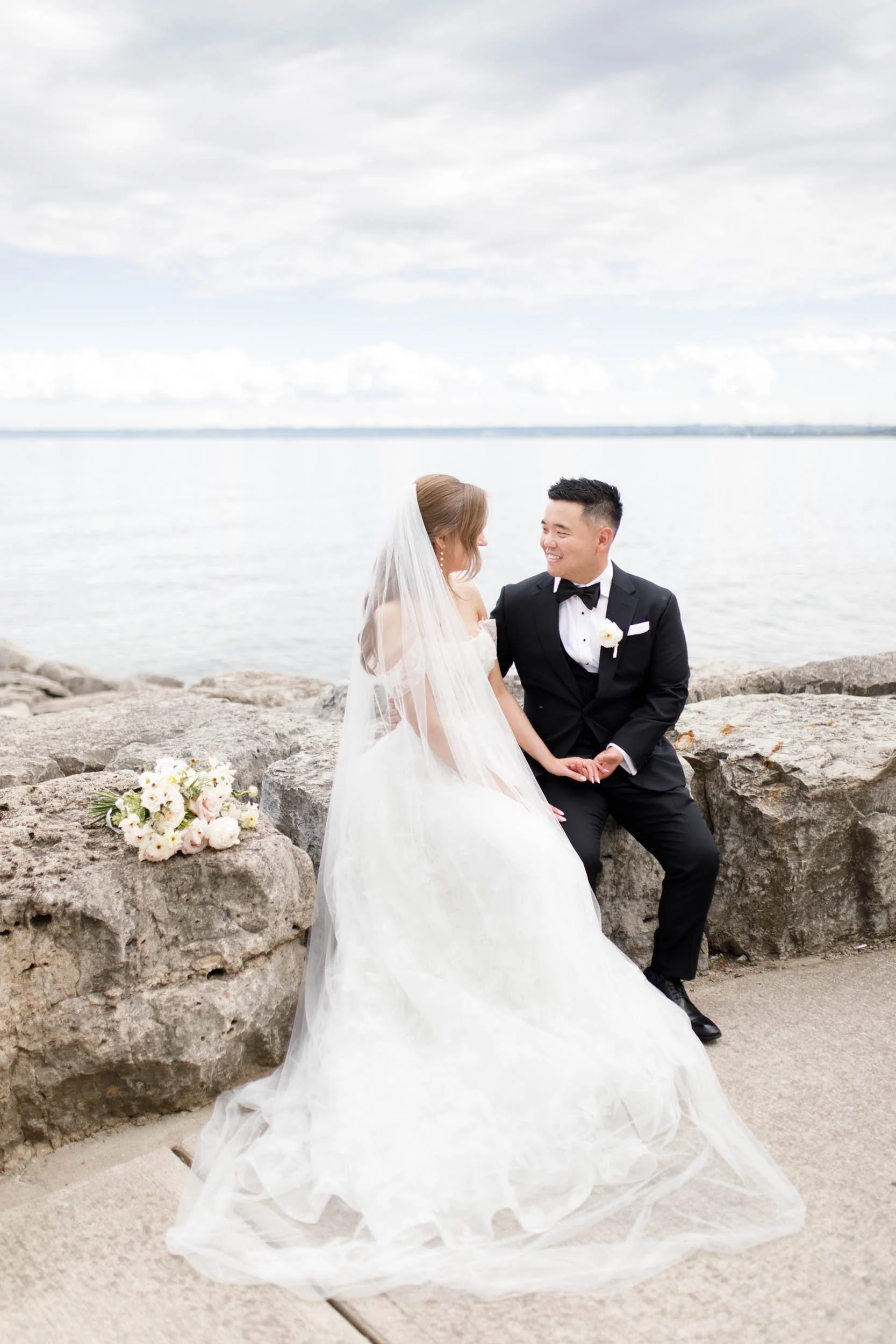 Bride and groom posing on the rocky shoreline at the Pearle Hotel in Burlington Ontario