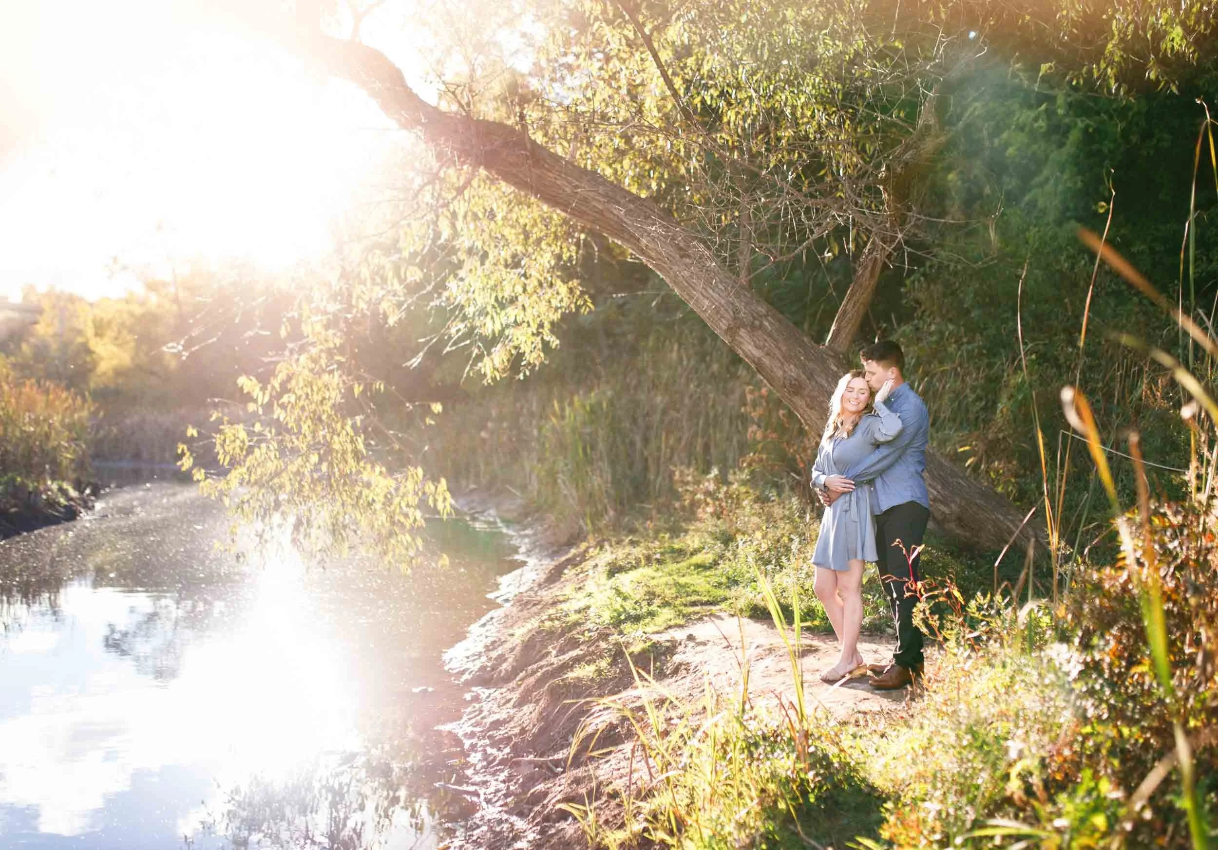 Wide engagement photo of a couple by the water at Grindstone Marsh Trail in Burlington Ontario at sunset