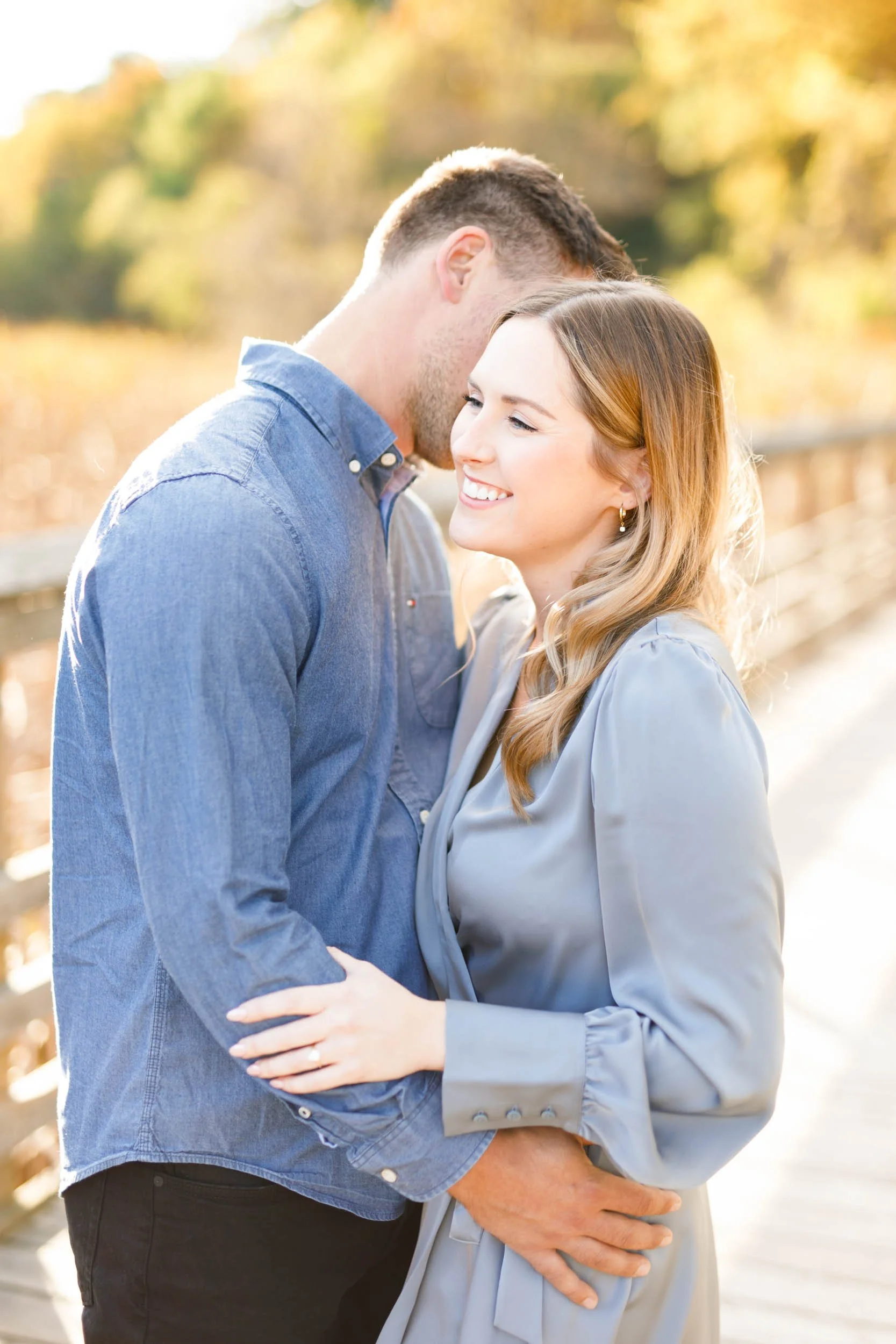 Bride-to-be smiling while being held by her fiancé during an engagement shoot at Grindstone Marsh Trail in Burlington Ontario