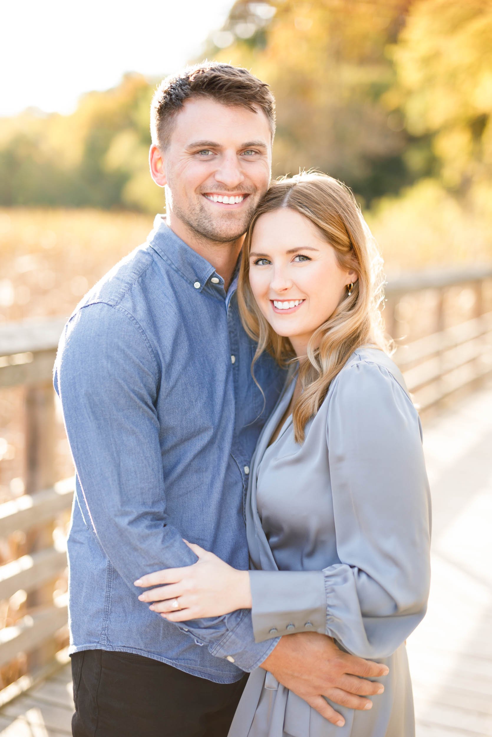 Engaged couple posing together on the boardwalk at Grindstone Marsh Trail in Burlington Ontario with autumn foliage