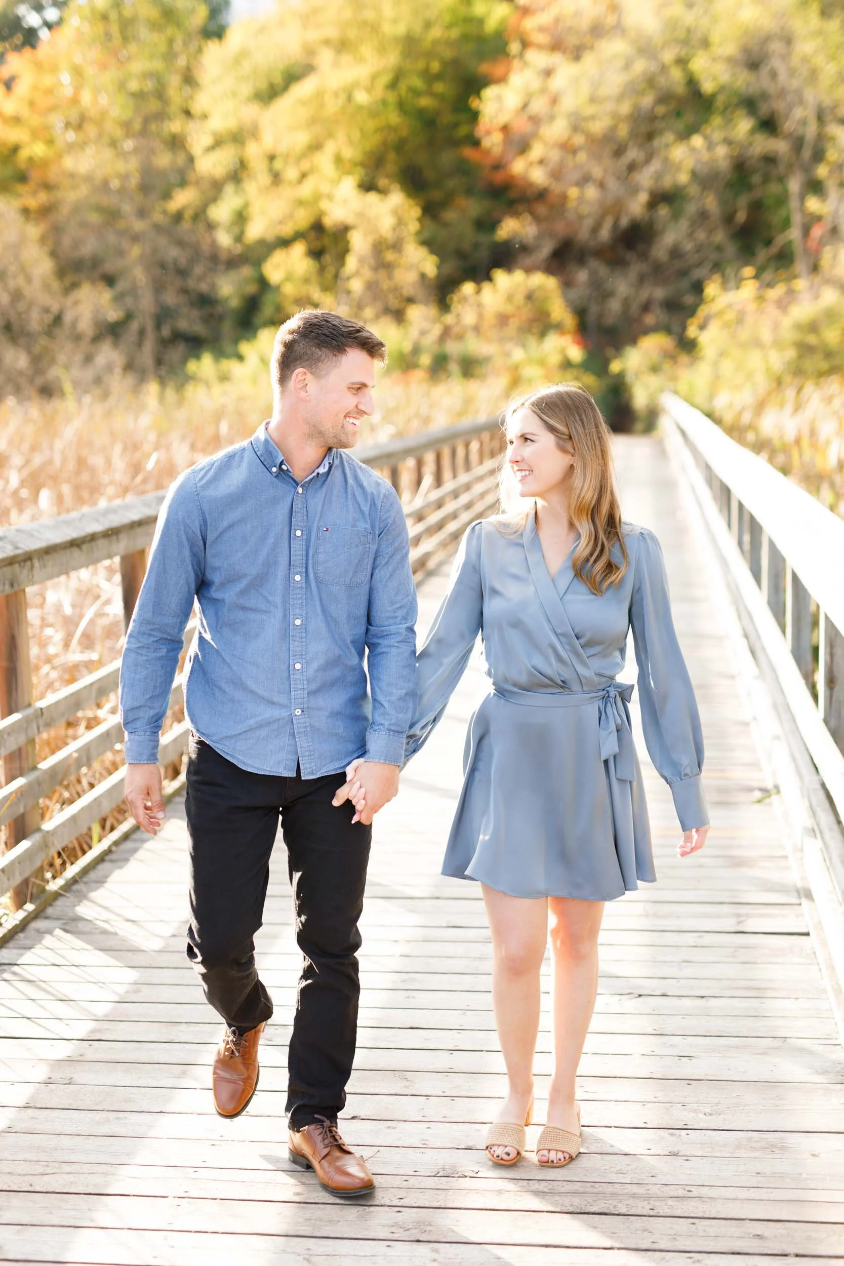 Engaged couple walking together on the boardwalk at Grindstone Marsh Trail in Burlington Ontario during their engagement shoot
