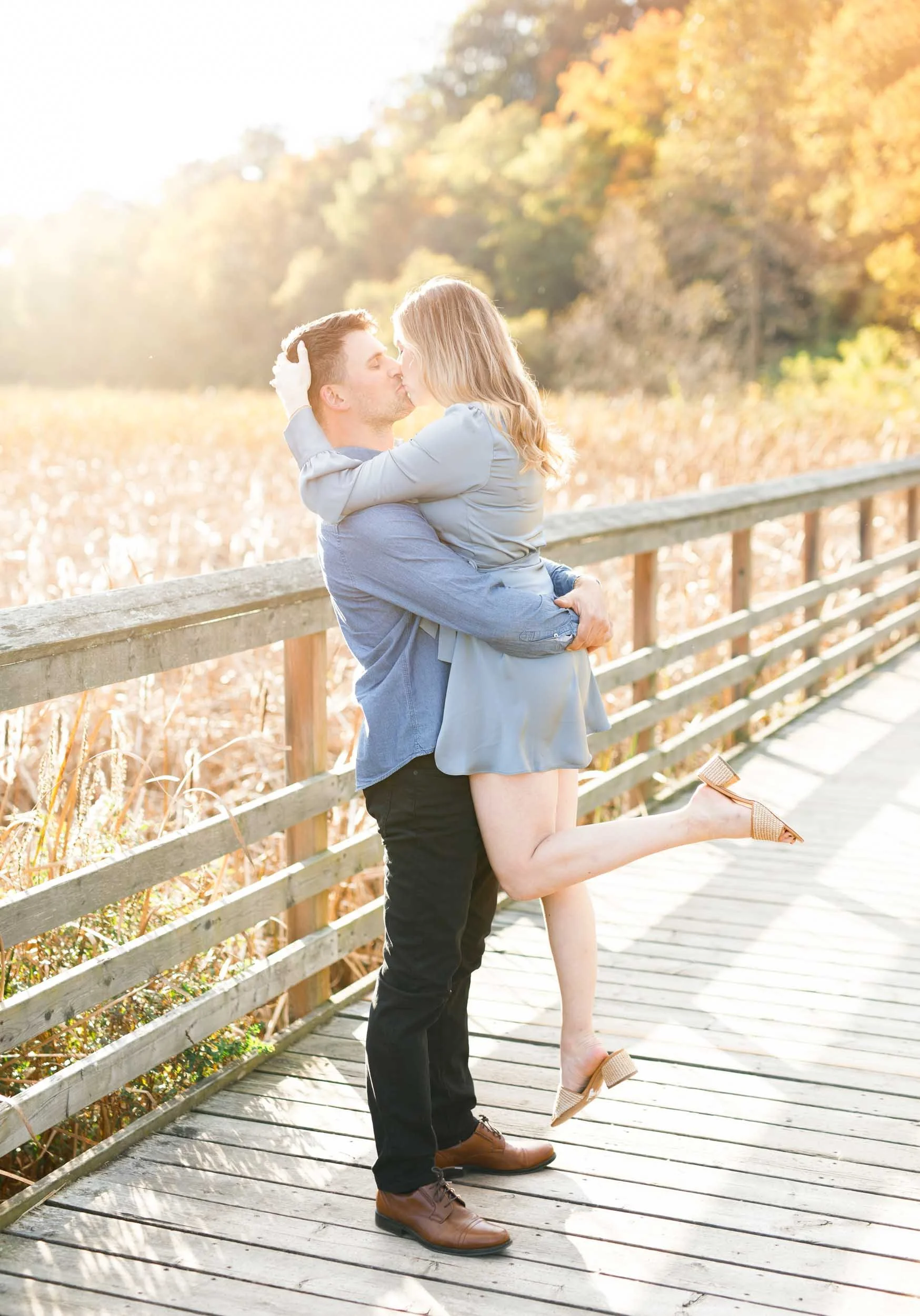 Couple hugging on a wooden boardwalk during a fall engagement session at Grindstone Marsh Trail in Burlington Ontario