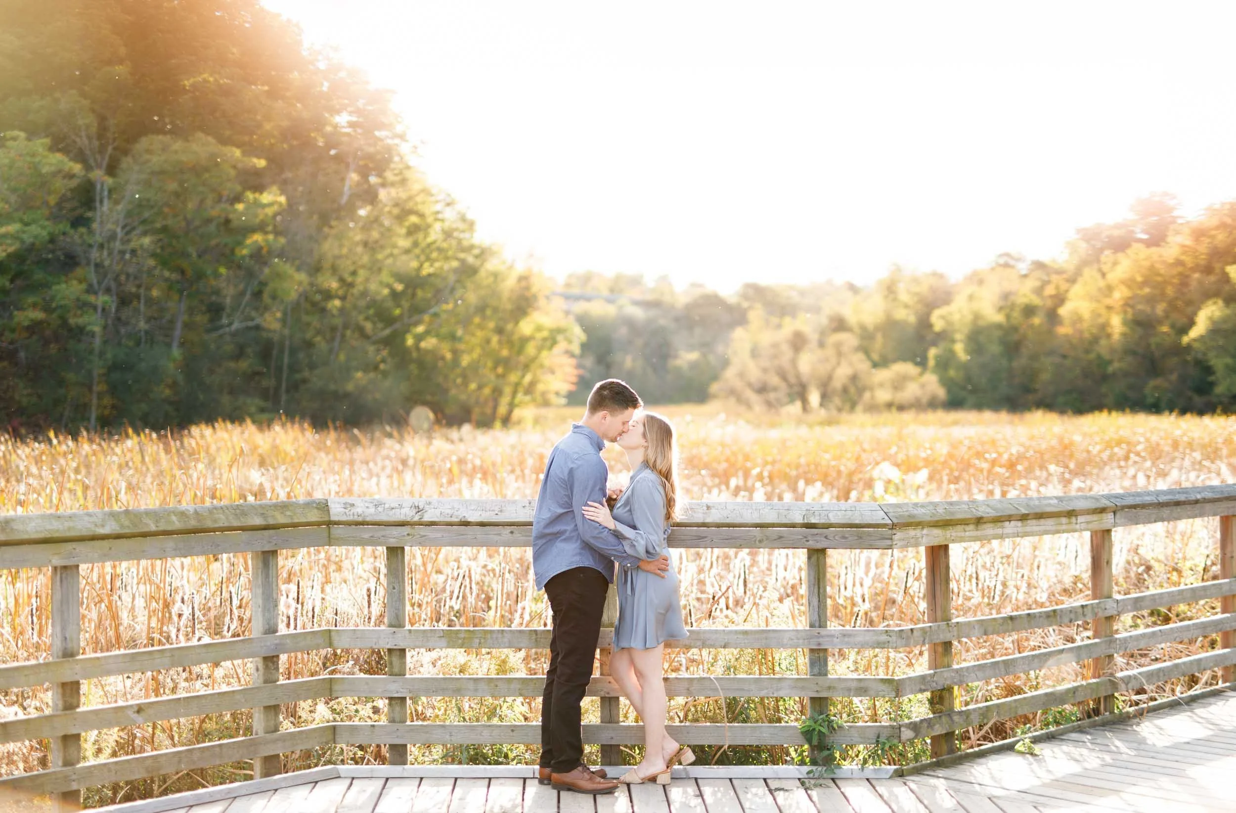Wide view of a couple standing together on the boardwalk at Grindstone Marsh Trail in Burlington Ontario during their engagement shoot