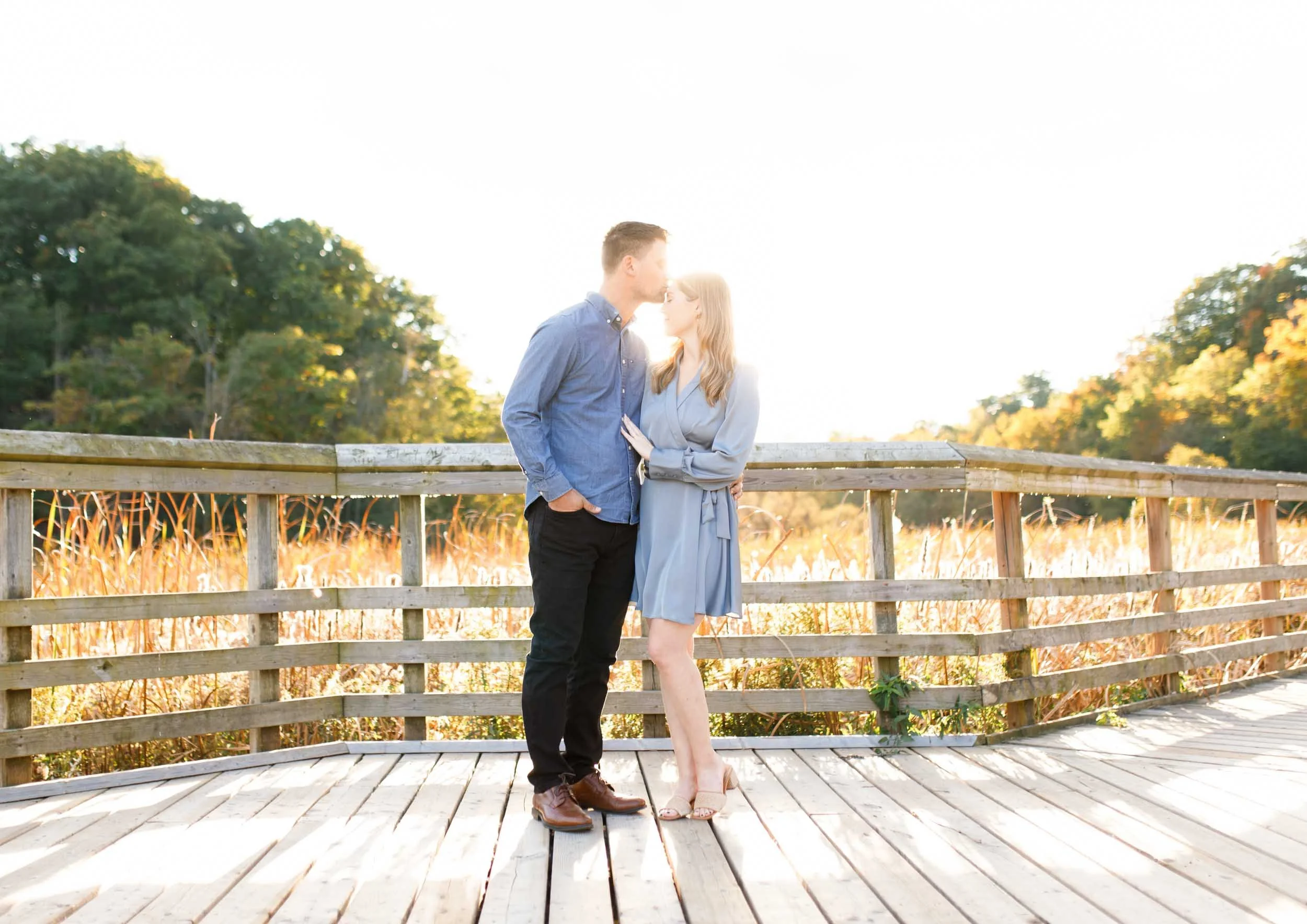 Engaged couple standing together on the boardwalk at Grindstone Marsh Trail in Burlington Ontario during an autumn engagement shoot