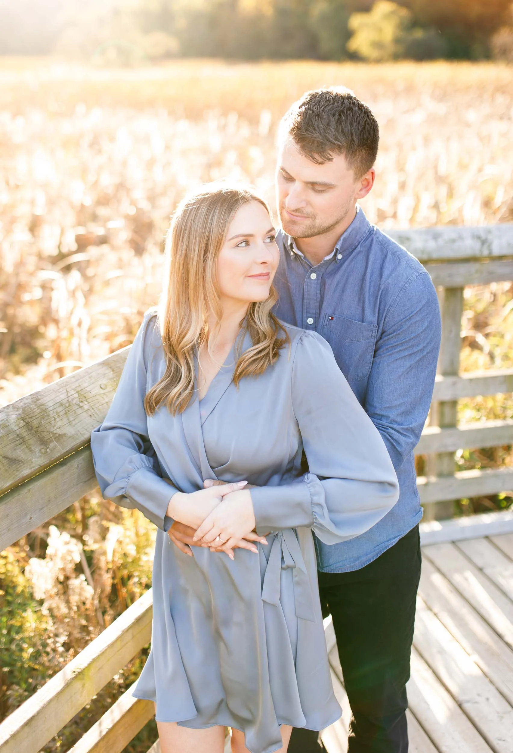 Engagement portrait of a couple leaning on the boardwalk railing at Grindstone Marsh Trail in Burlington Ontario