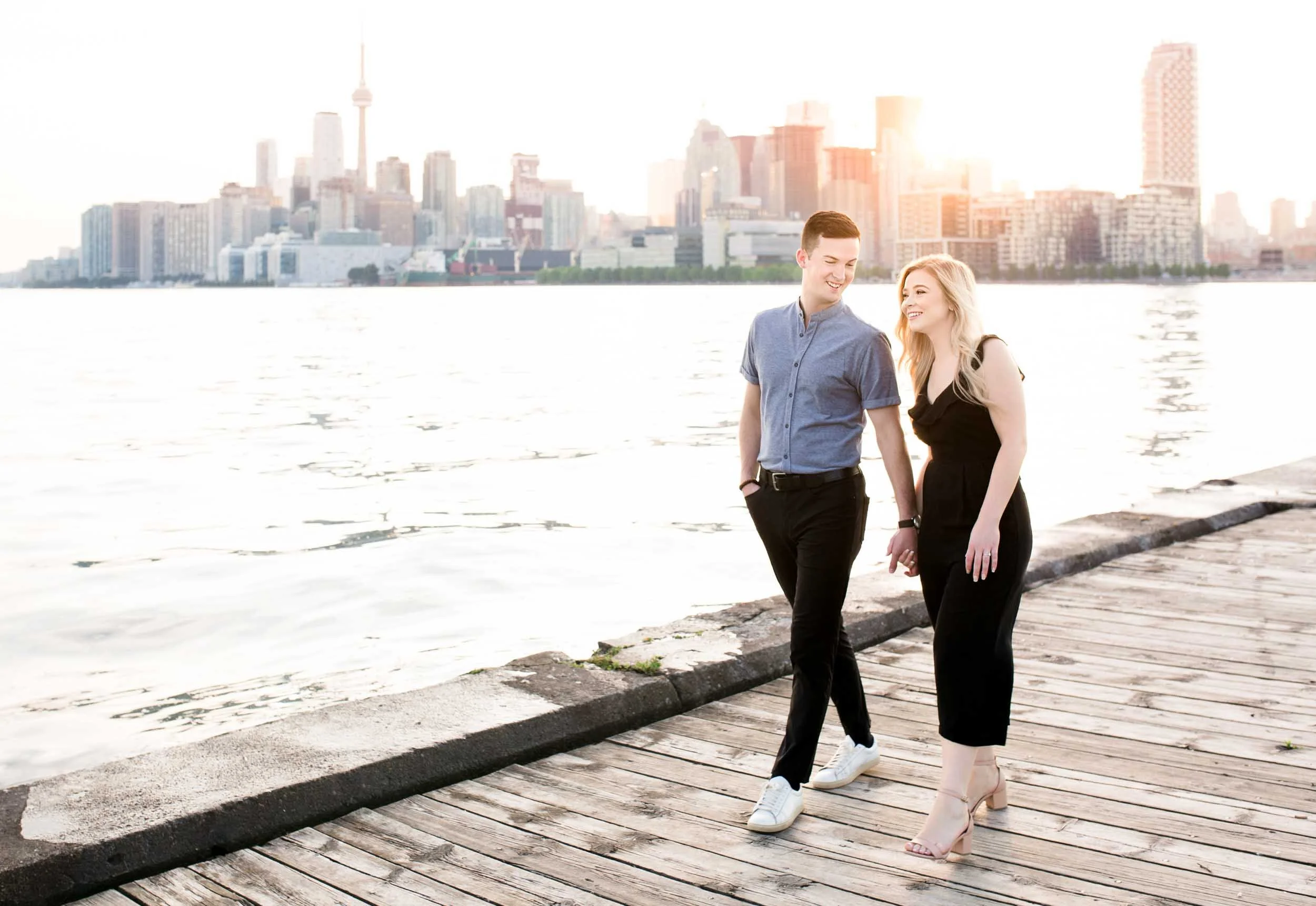 Engaged couple walking along the Toronto waterfront pier with the city skyline behind them (Copy)
