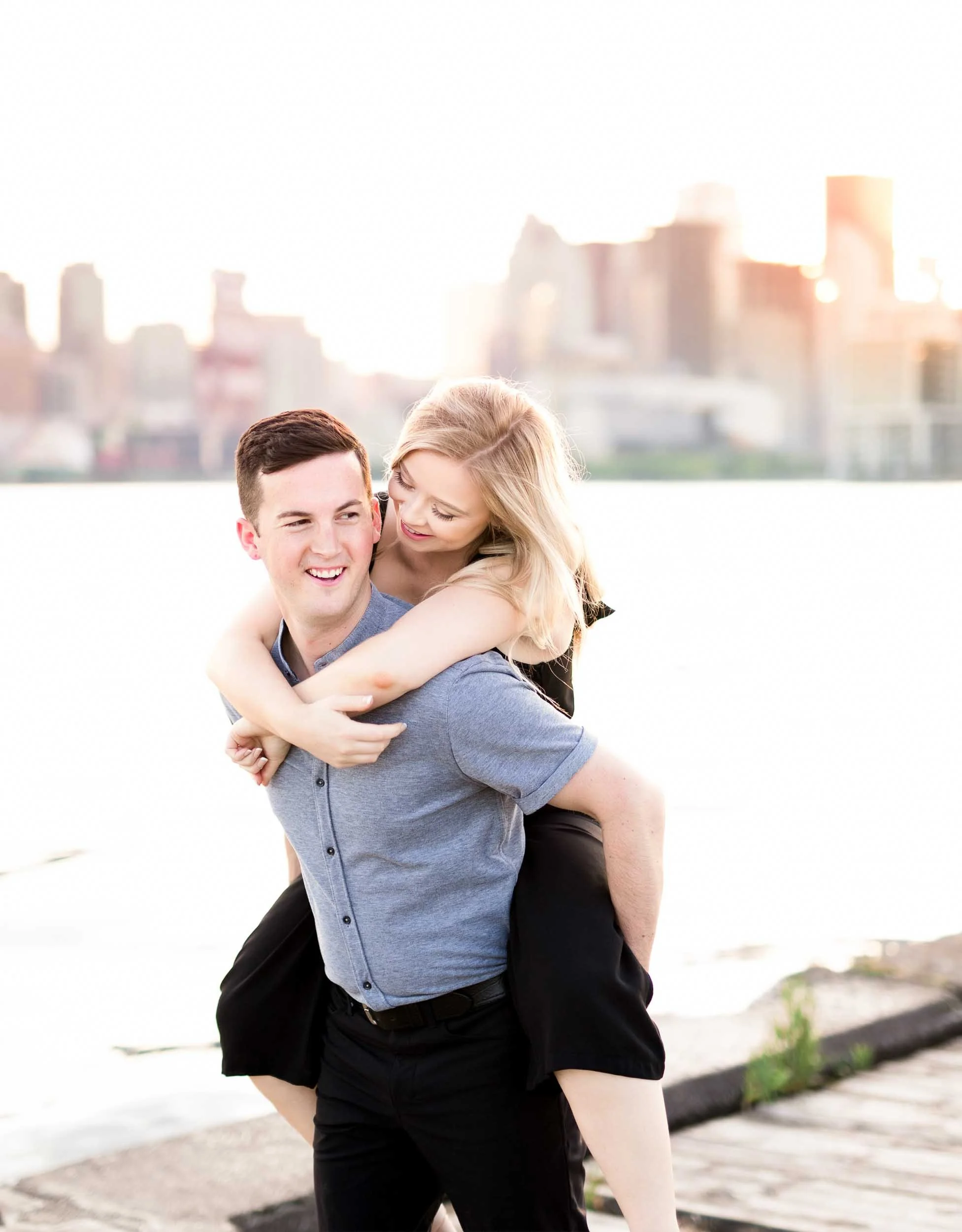 Engaged couple piggy-backing along the waterfront with Toronto skyline softly blurred in the background (Copy)